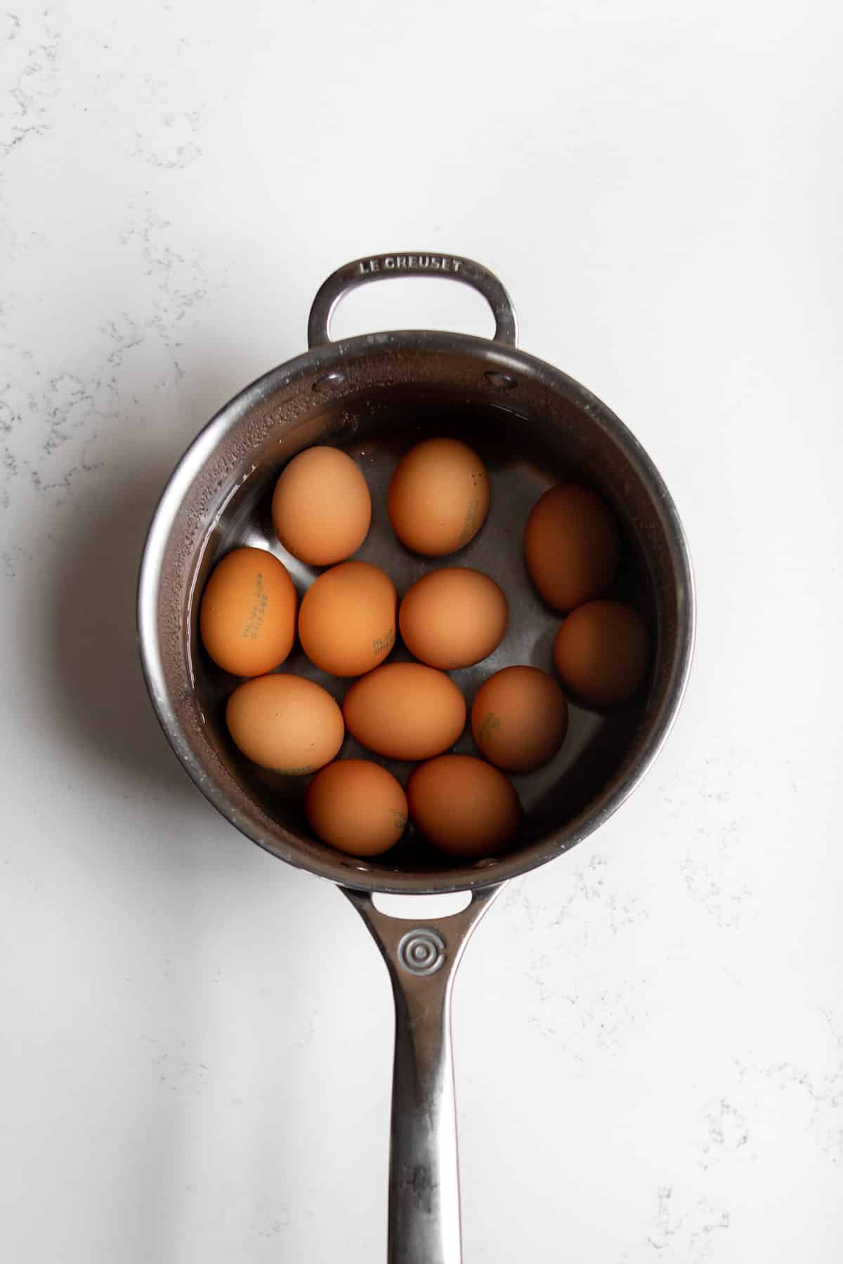A dozen eggs in a stainless steel pot submerged in water.