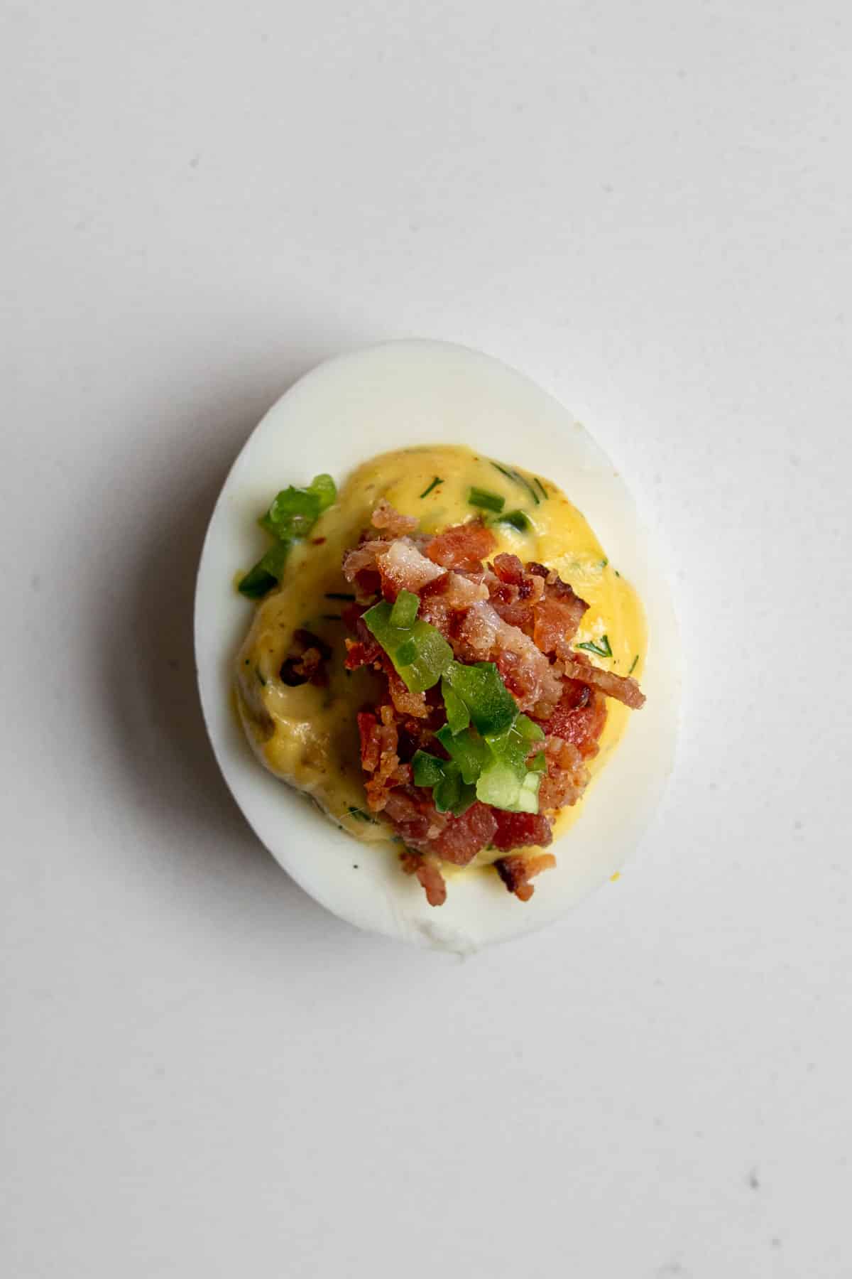 Close up of a spicy devilled egg topped with bacon and jalapeno