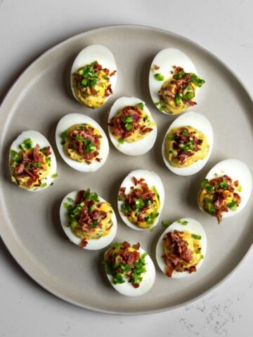 Spicy devilled eggs on a beige plate topped with bacon and jalapeno.