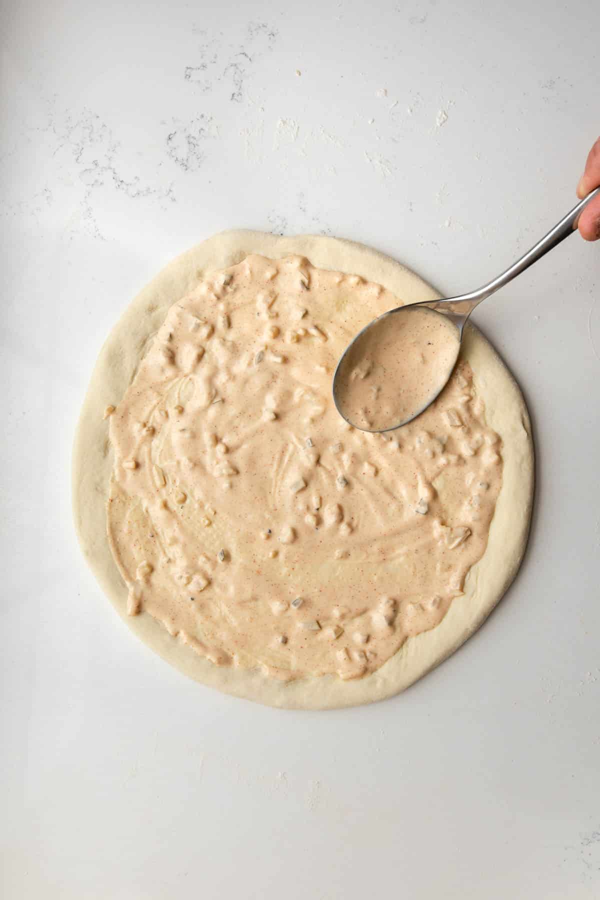 PIzza dough rolled out in a circle on a marble table with Big Mac Sauce spooned out over it.