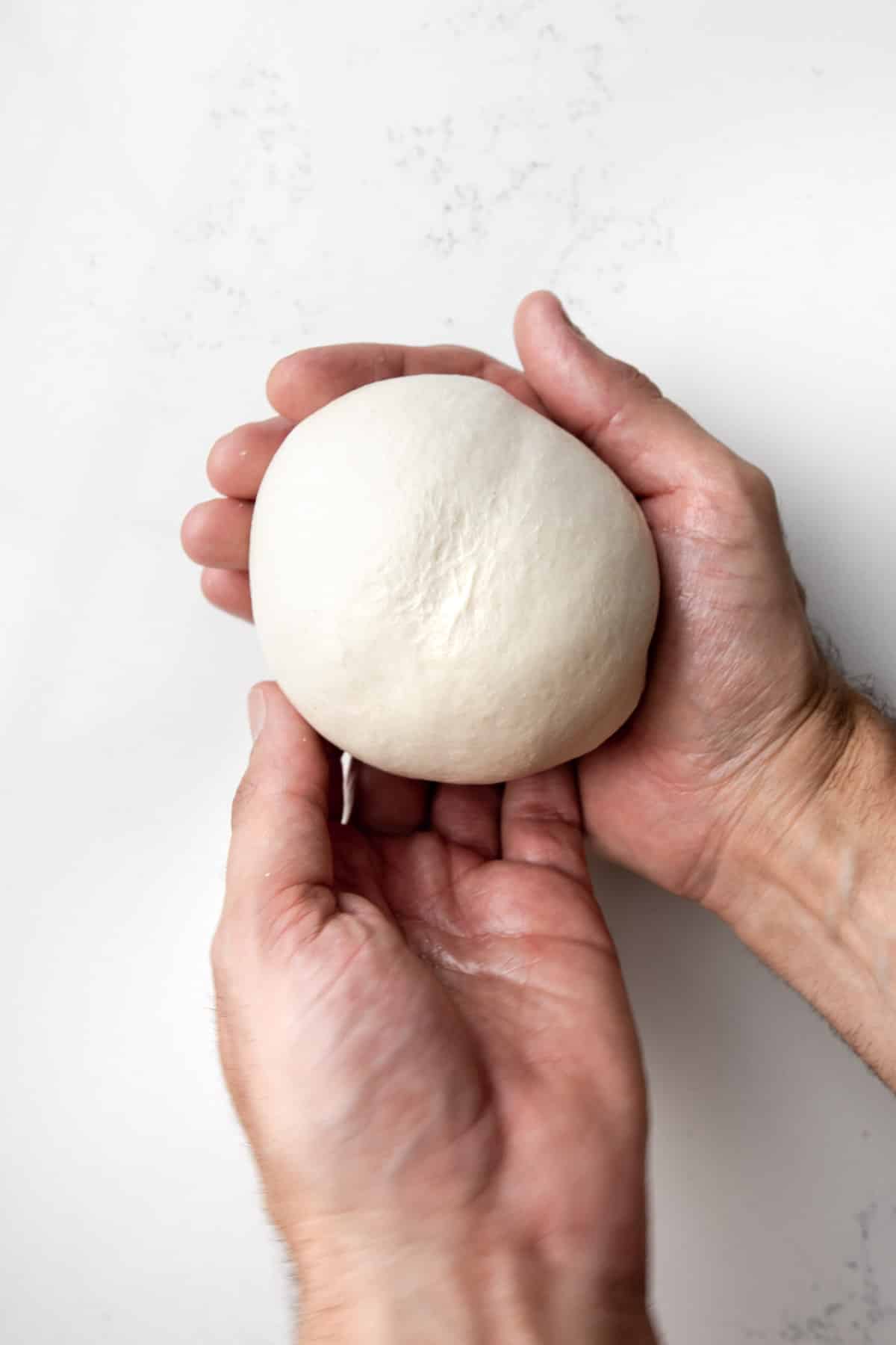 Rolled pizza dough in the palm of a man's hand.