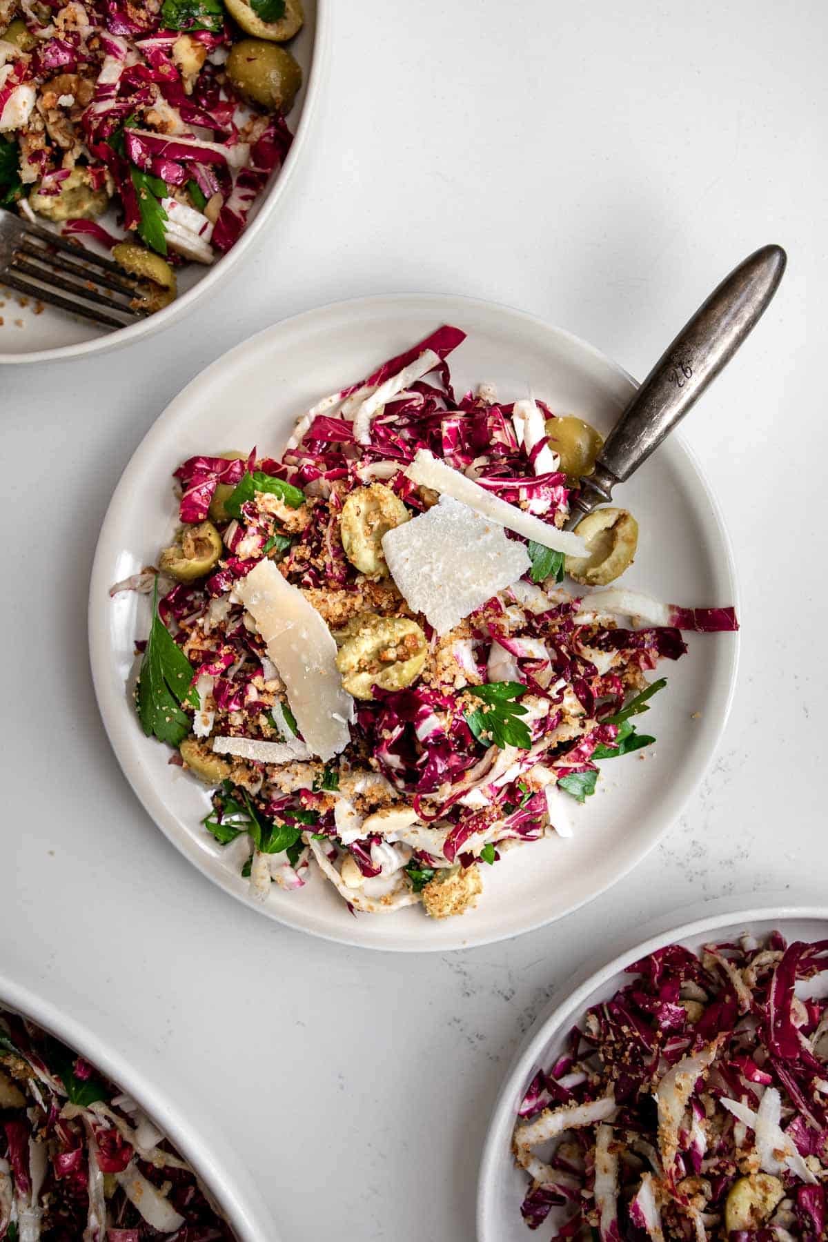 Three plates on a table with radicchio salad in them and a fork.
