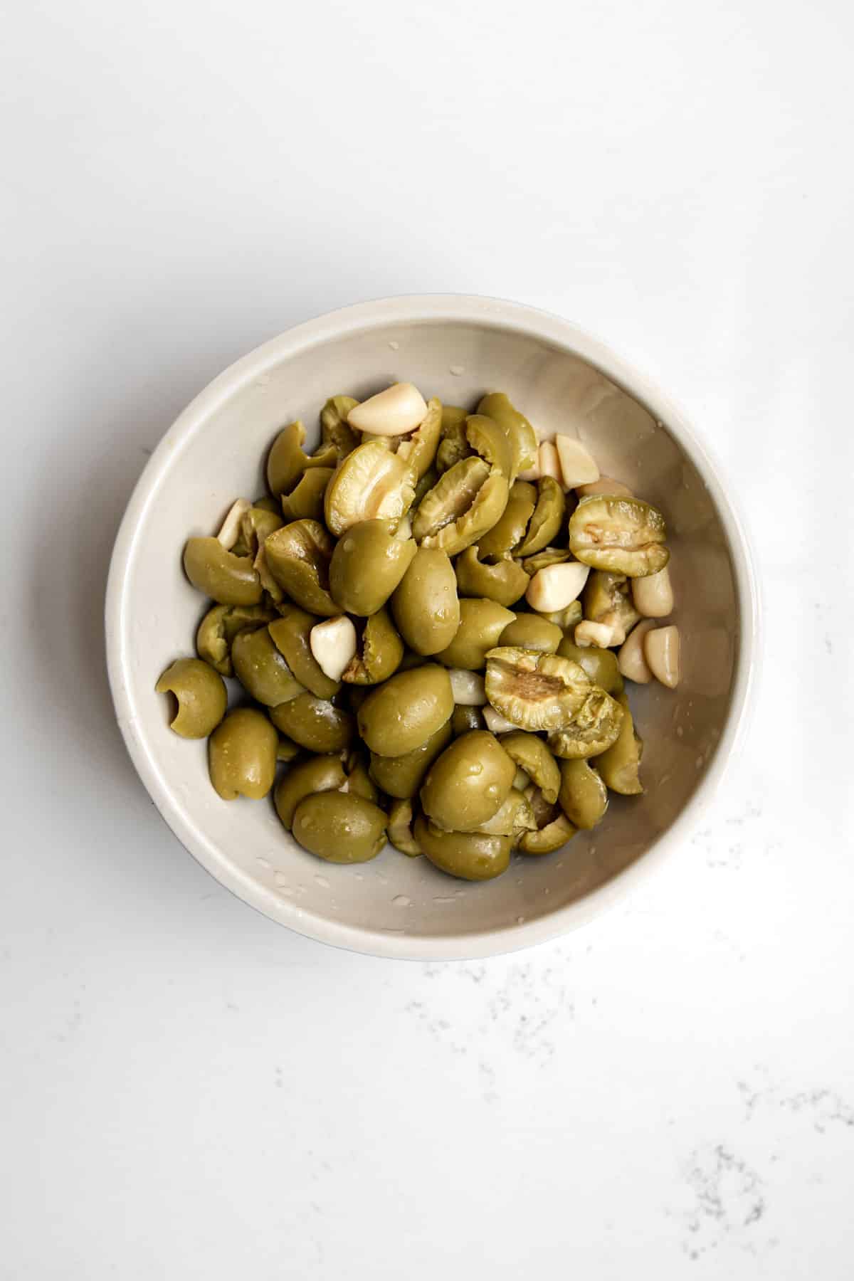Beige bowl of olives torn with garlic cloves on a white table for radicchio salad.