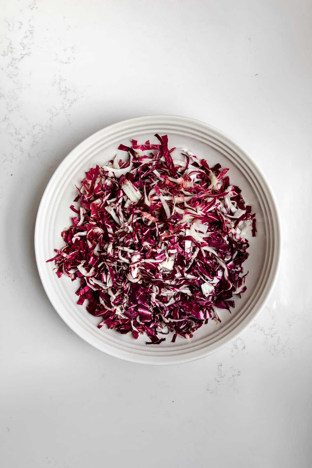 Shredded radicchio in a large white bowl on a white table.