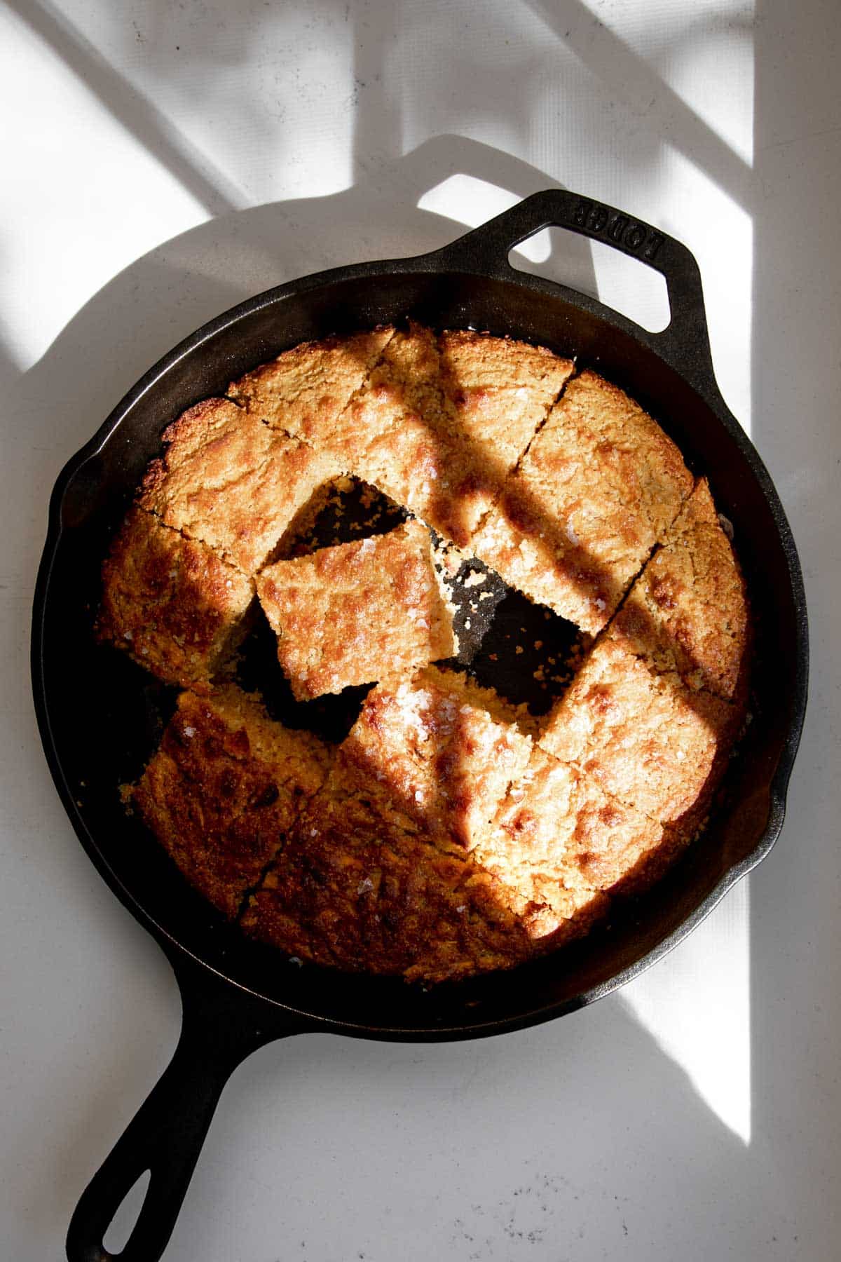 Cornbread cut in squares in a cast iron skillet with shadows casting overtop.