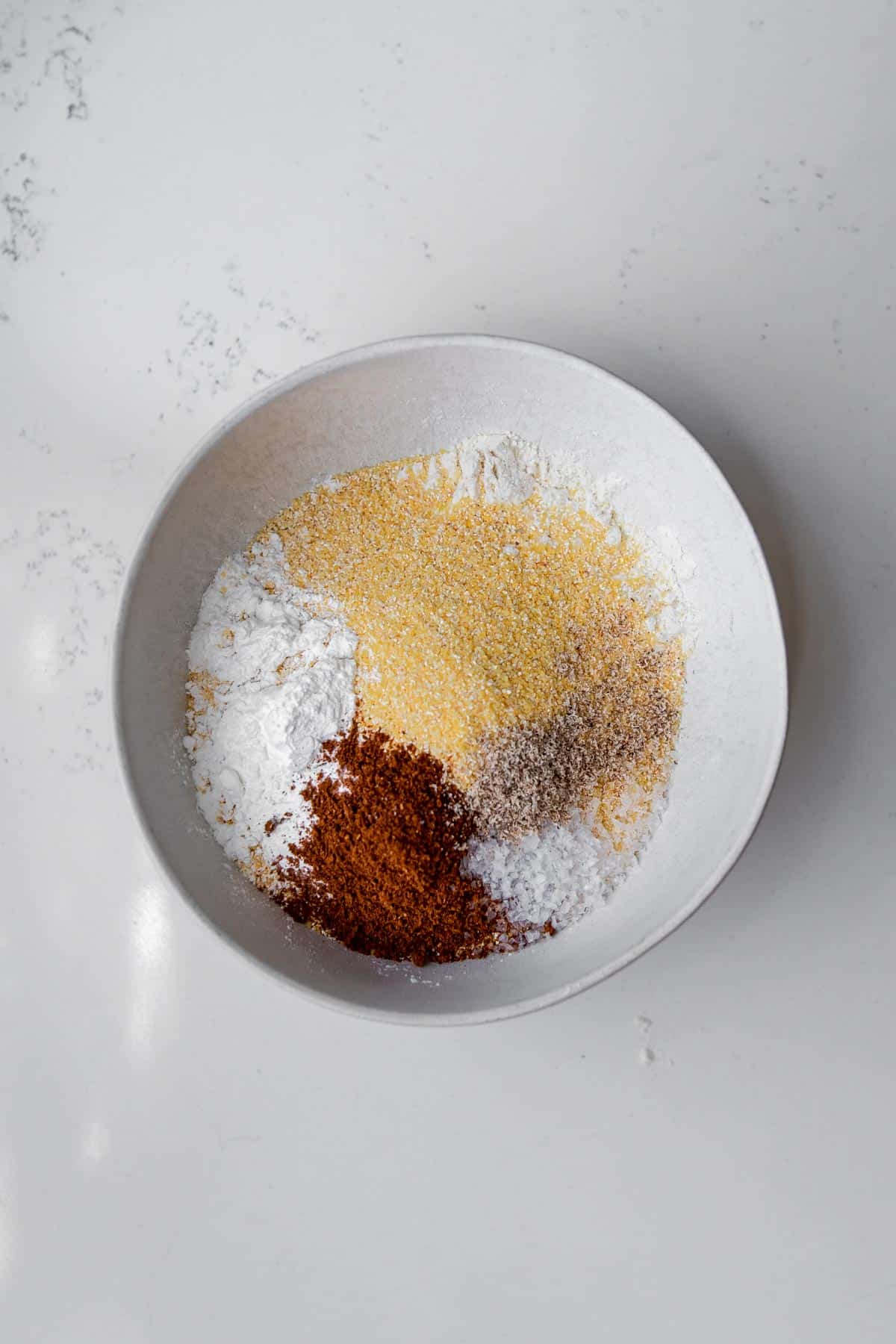 Flour, cornmeal, baking powder, cinnamon, nutmeg, and salt in a white bowl.