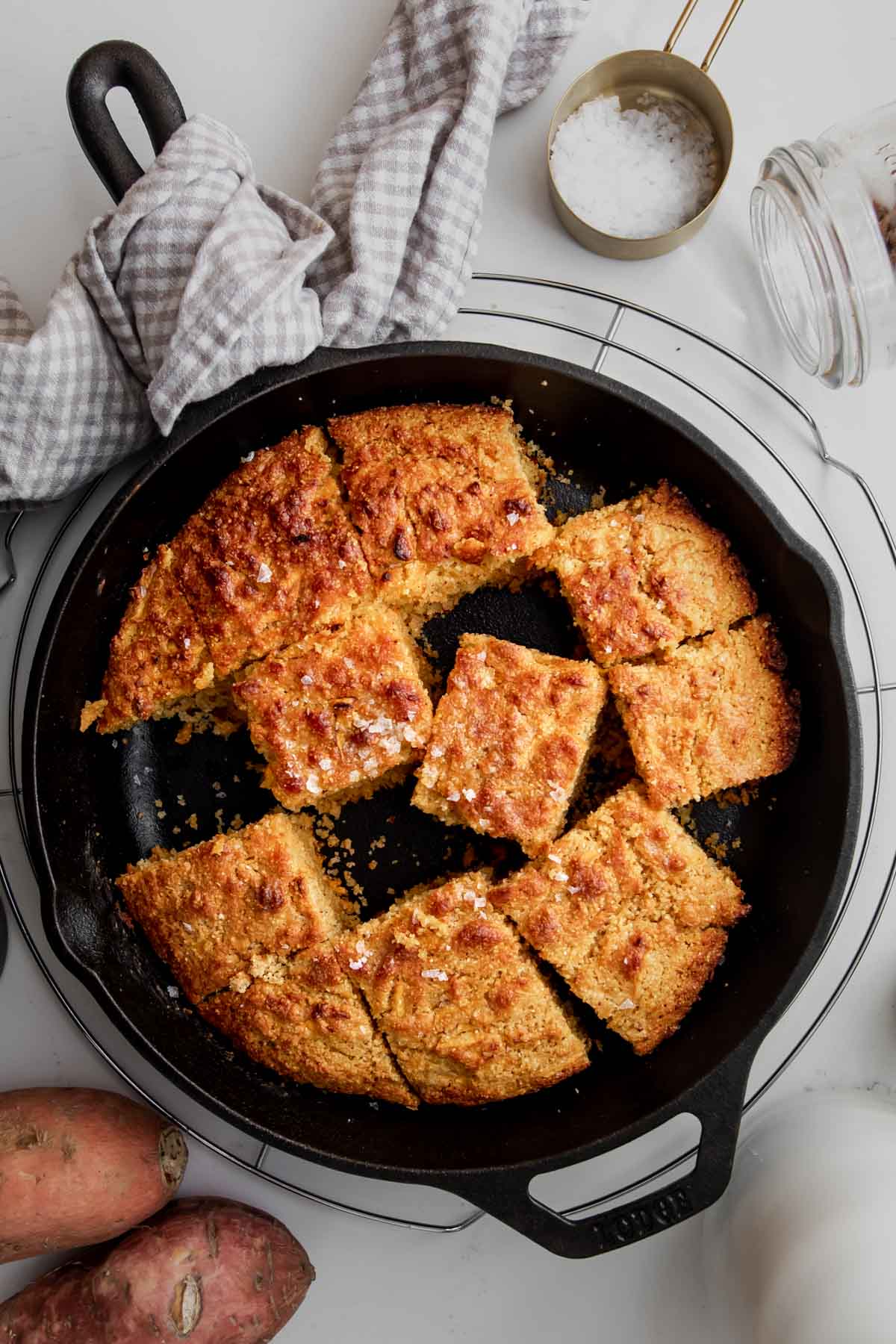 Cornbread cut in squares in a cast iron skillet placed on a wire rack.