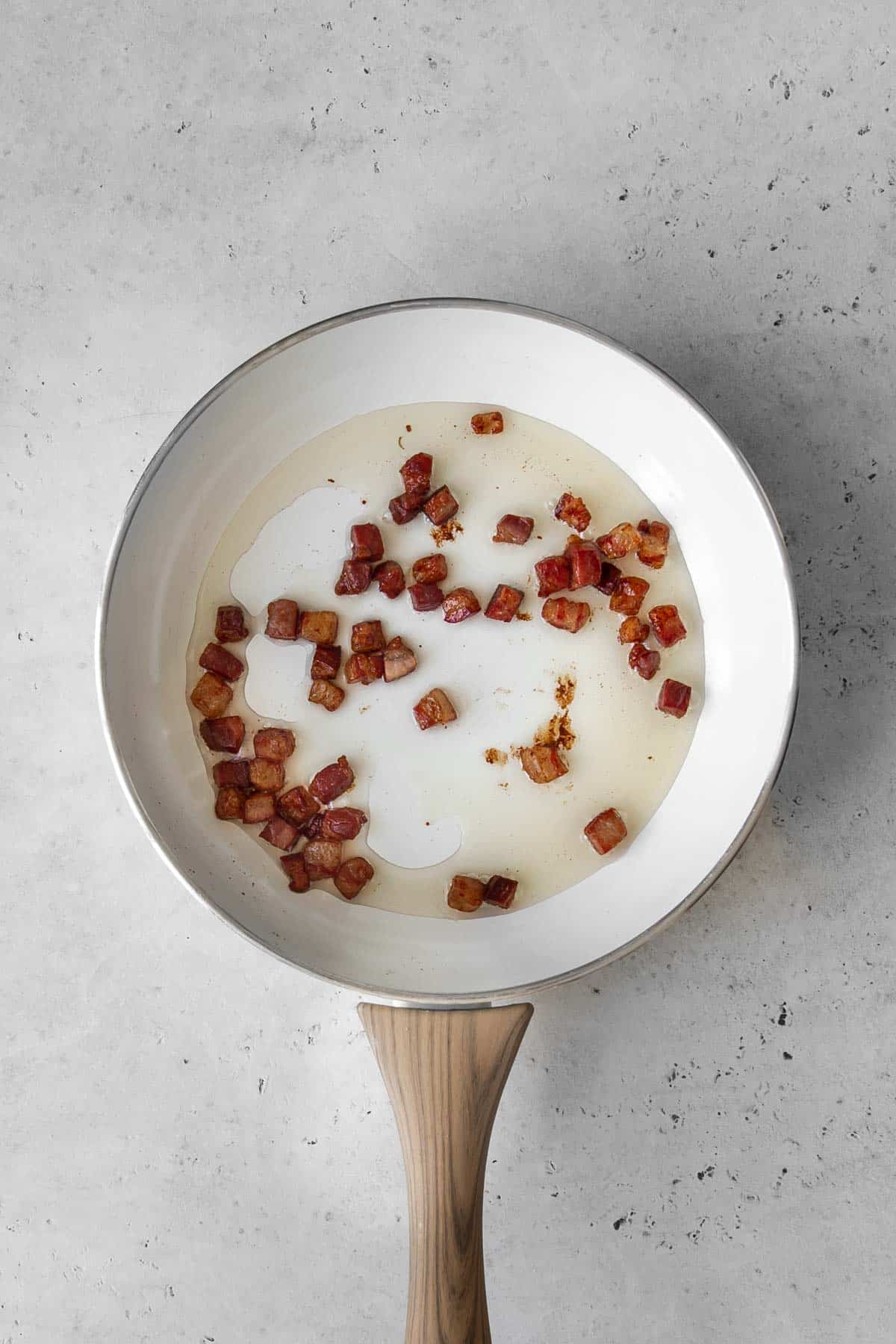 Crispy pancetta arranged in a white pan with wooden handle on table.