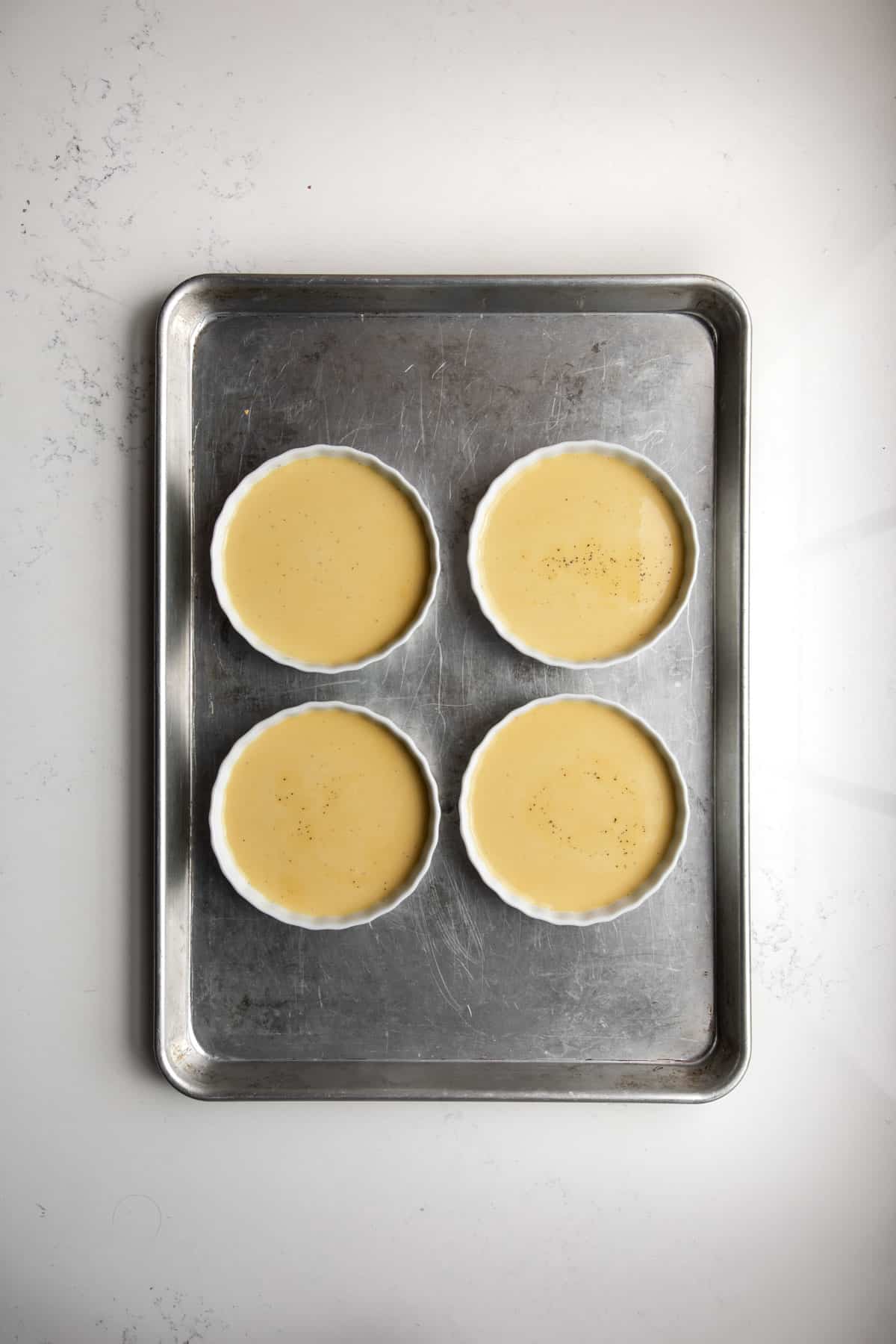 4 ramekins on a baking sheet with custard mixture.
