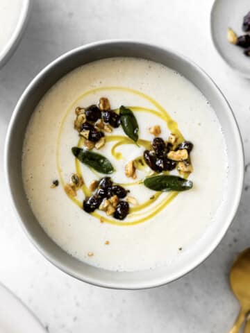 Bowl of creamy cauliflower soup topped with a drizzle of olive oil, sage, raisins and walnuts.