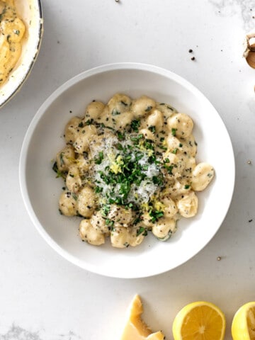 Gnocchi in lemon cream sauce in a white pasta bowl on a marble table topped with basil and lemon.