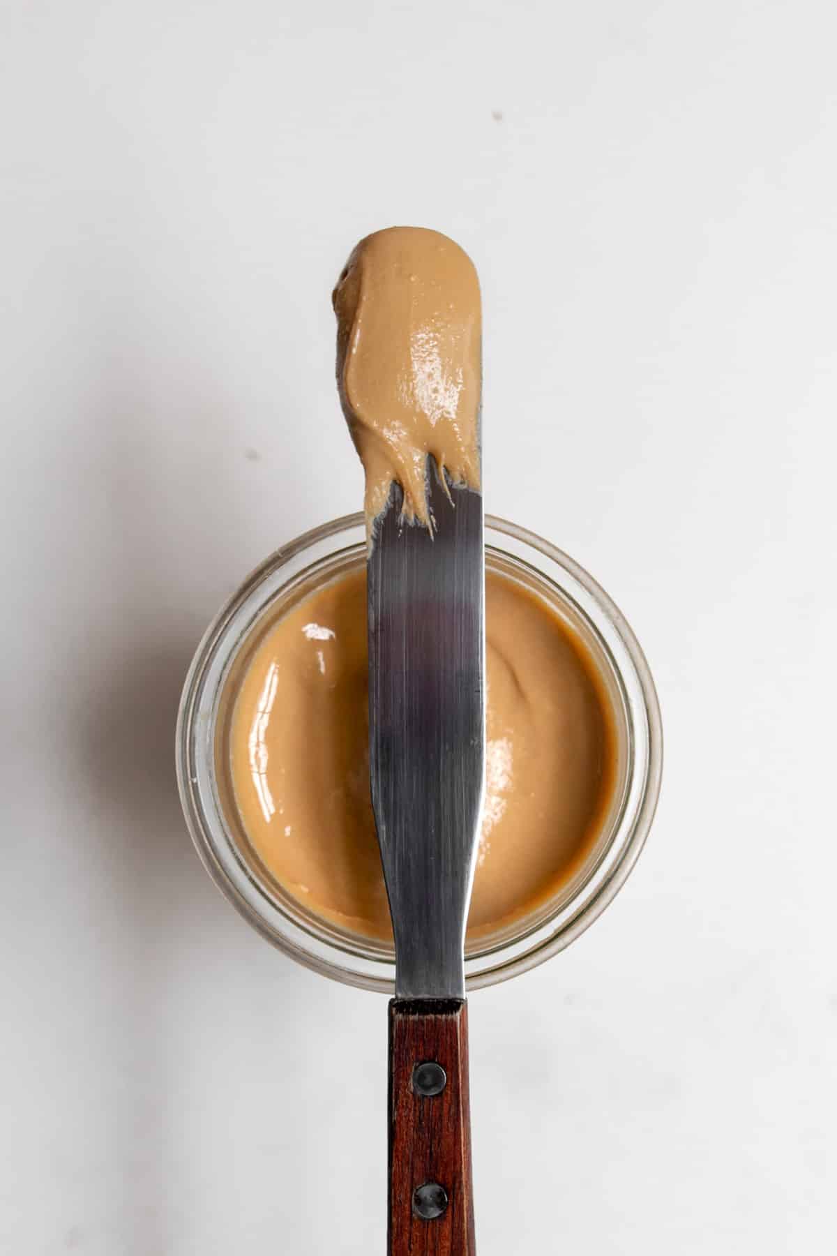 Overhead view of smooth and creamy cashew butter on a spreading knife placed on top of a glass jar of cashew butter.