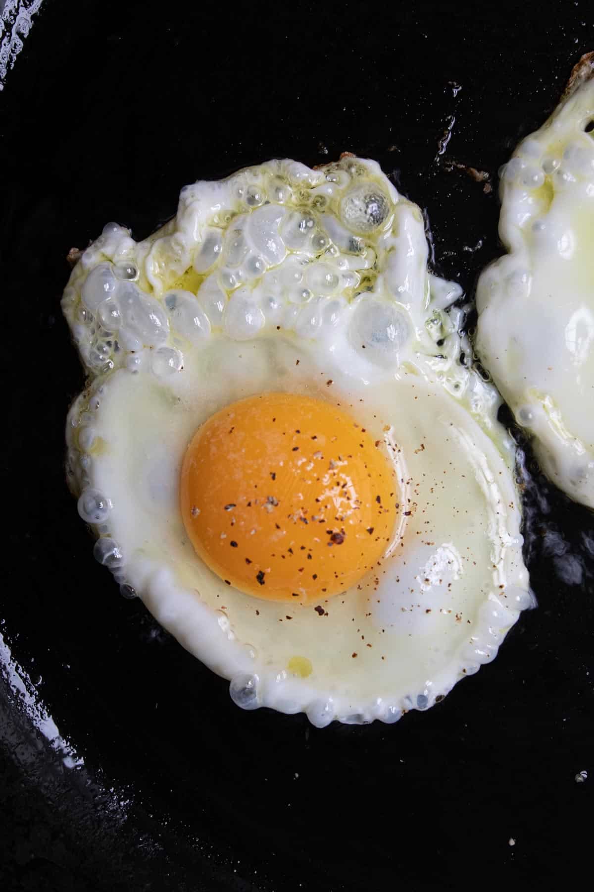 Close up of an egg frying on a cast iron skillet.