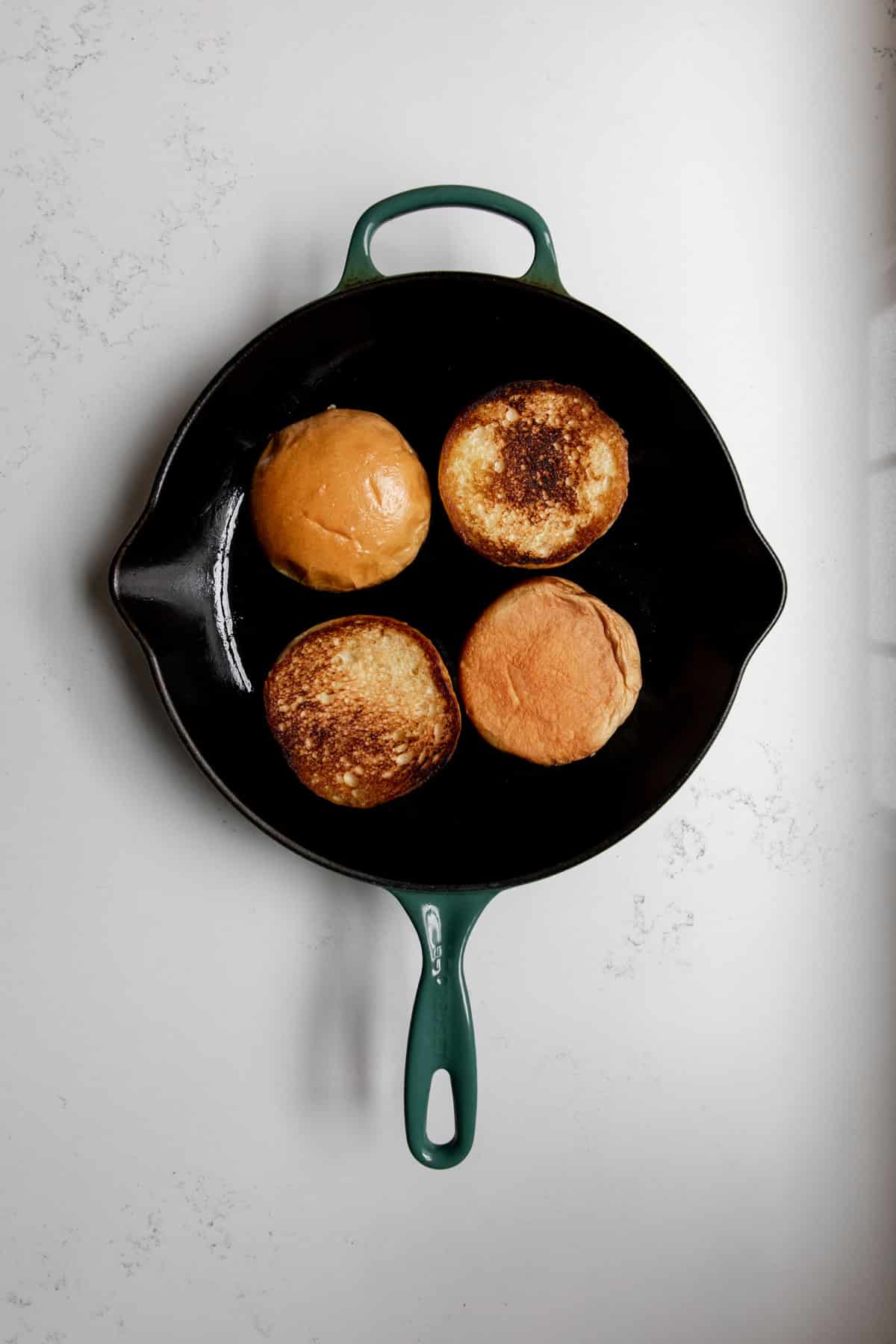 Four toasted brioche buns in a cast iron skillet.