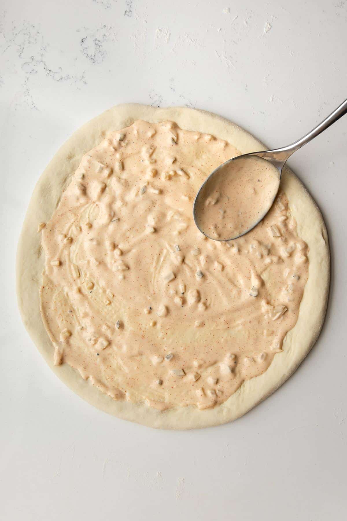 spoon adding big mac sauce to rounded pizza dough.