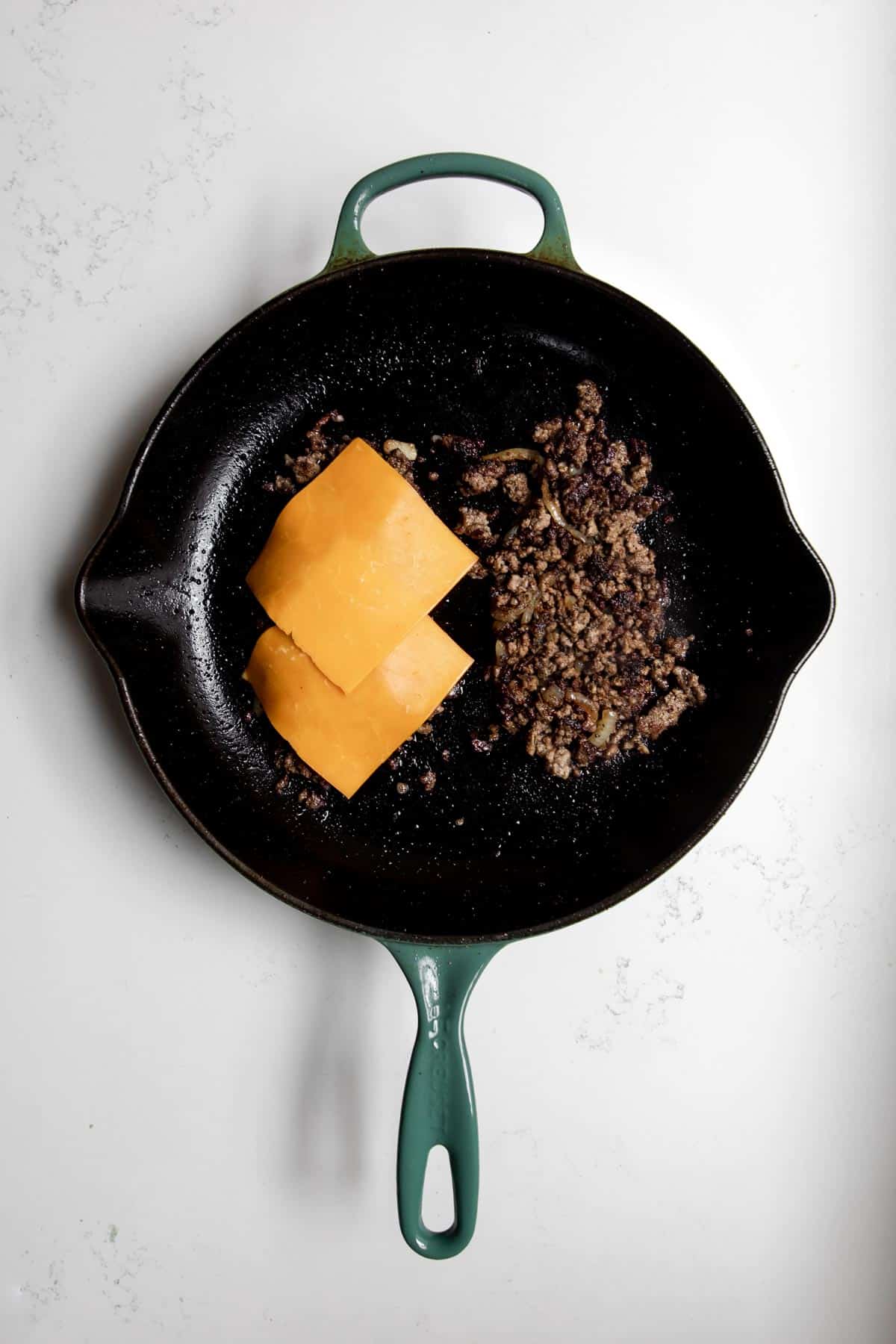 Ground beef cooking in a cast iron skillet topped with cheese.