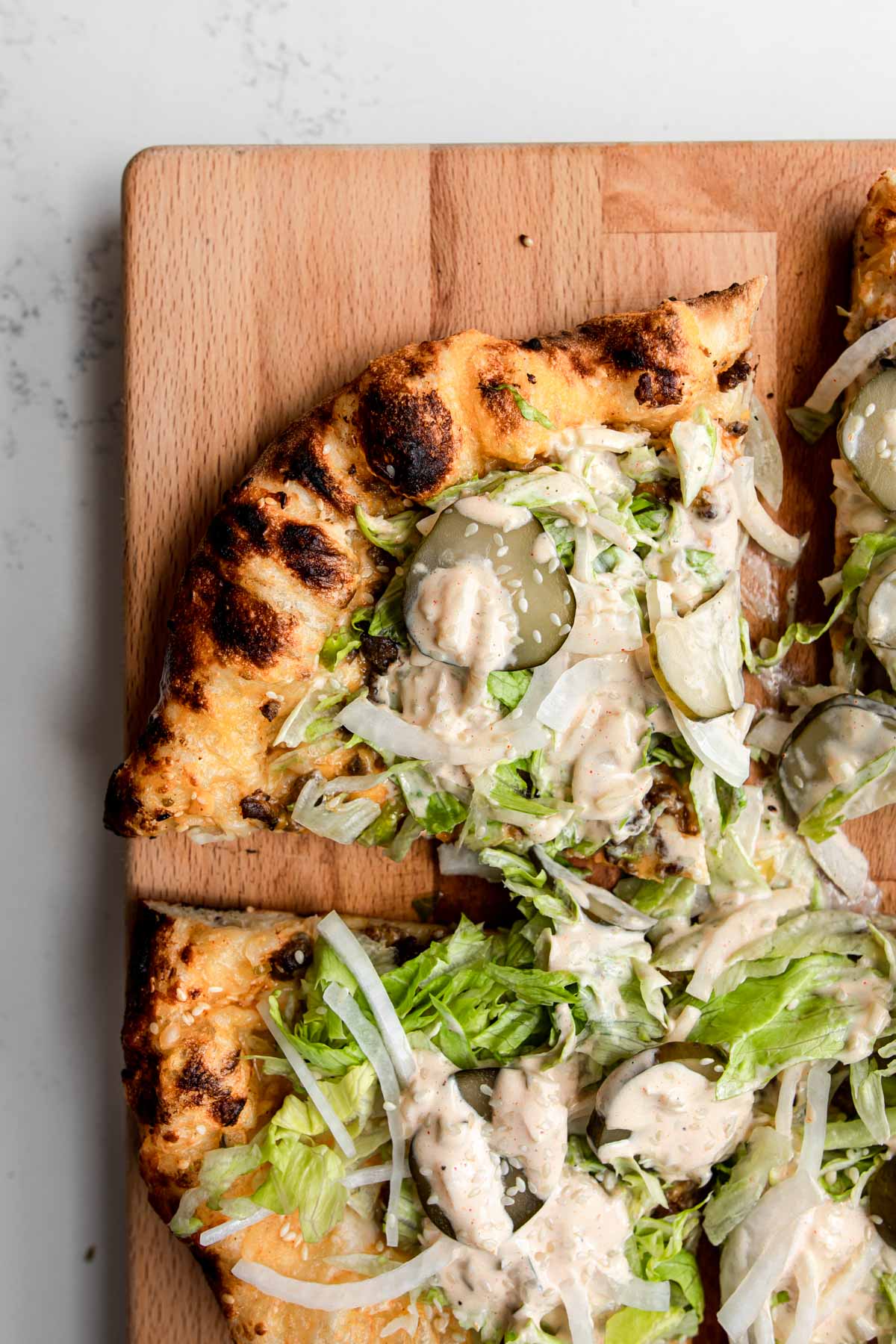 close up of oven baked pizza topped with pickles, lettuce, onion, mac sauce and sesame seeds.