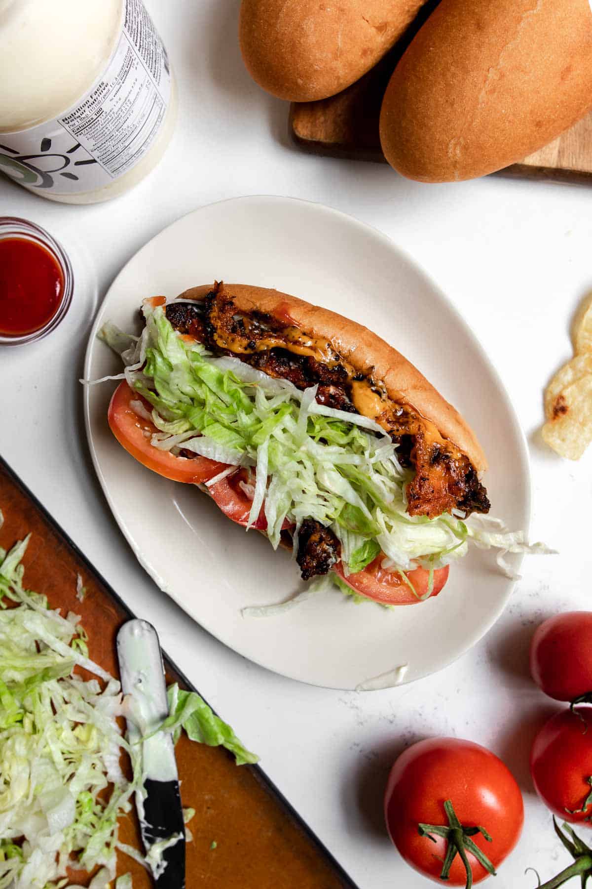 Chopped cheese sandwich topped with tomato and iceberg lettuce on a white plate.