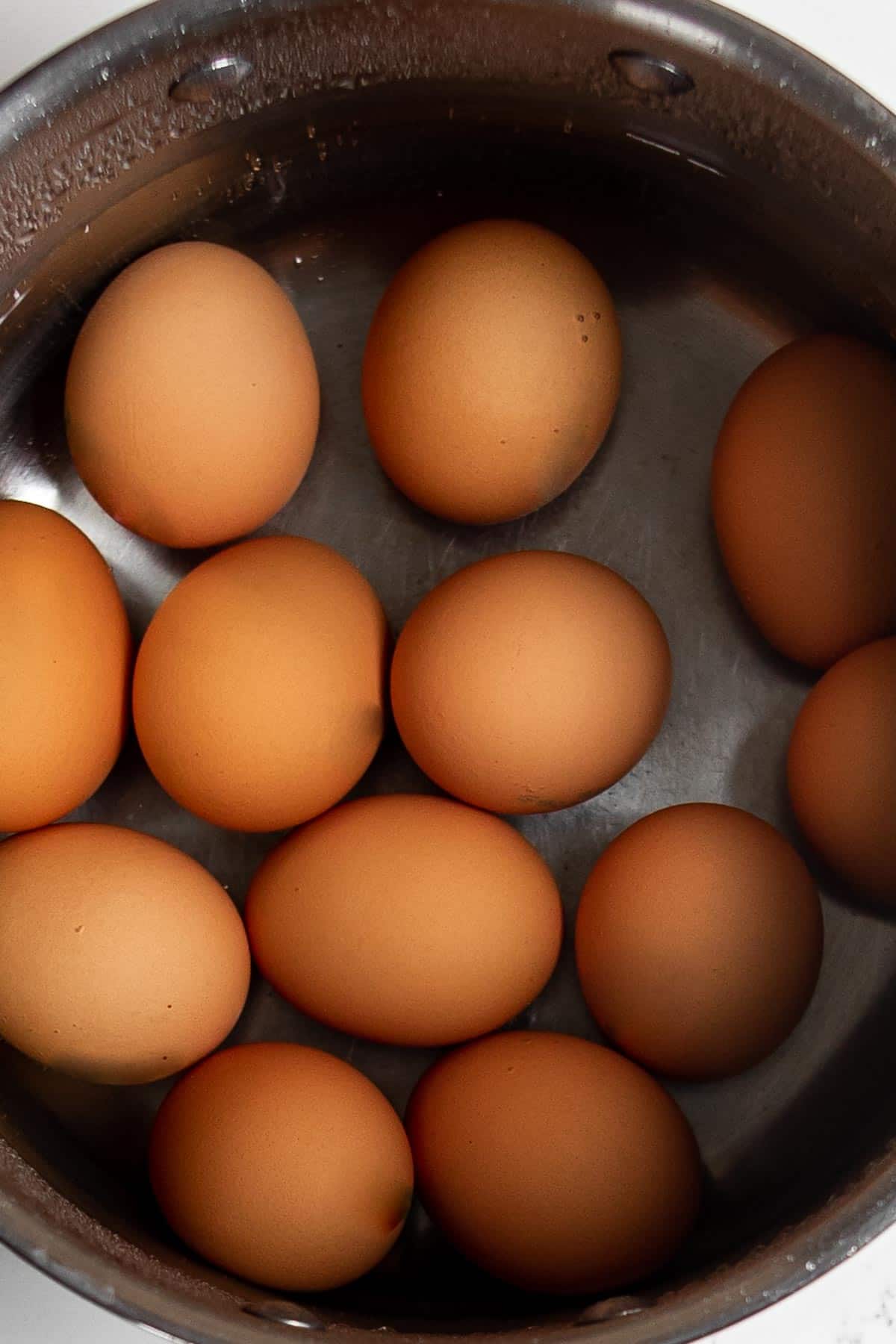 a dozen eggs in a pot of water on the stove.