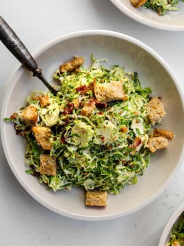 shaved brussels sprout caesar salad in a bowl with a fork.