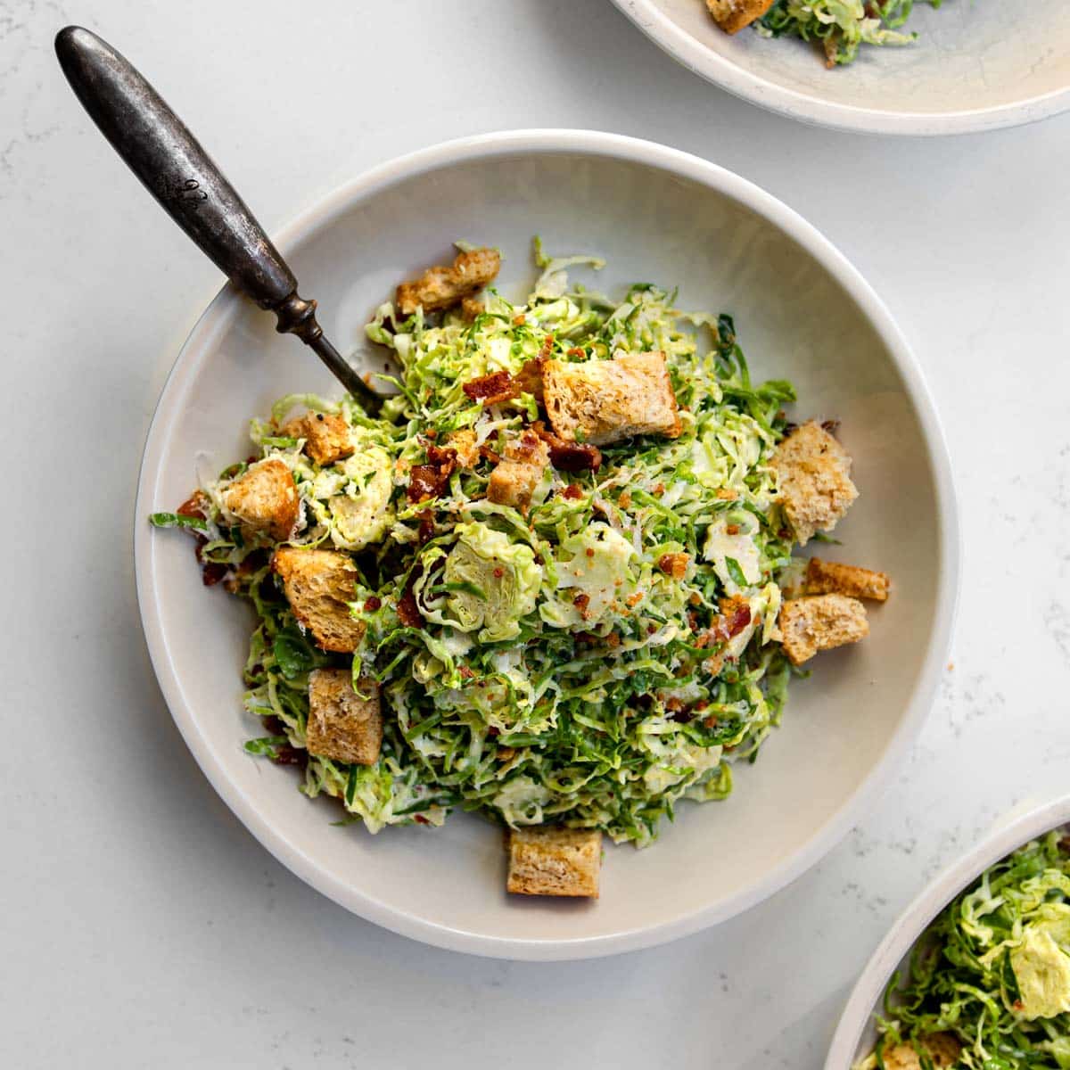 shaved brussels sprout caesar salad in a bowl with a fork.