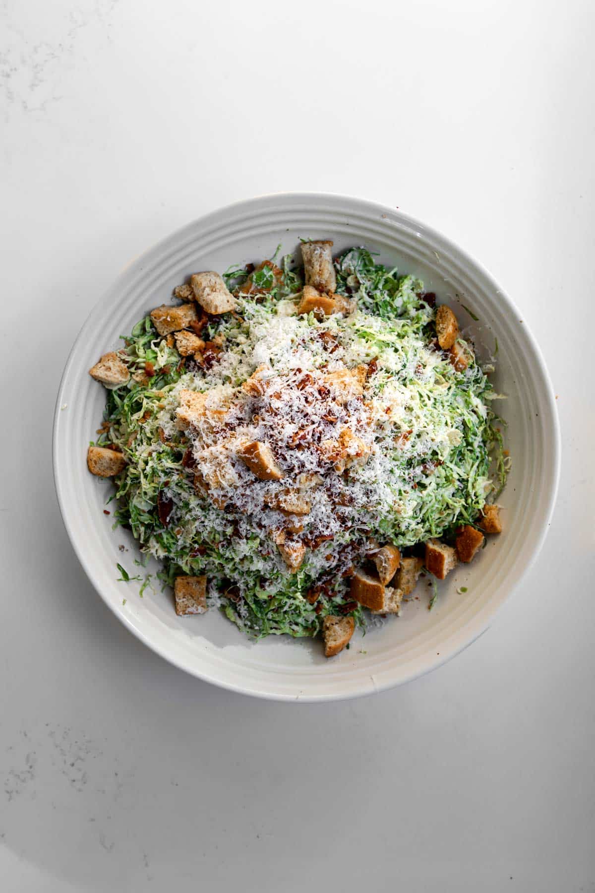 shaved brussle sprout caesar salad in a large bowl with grated parmesan over top.