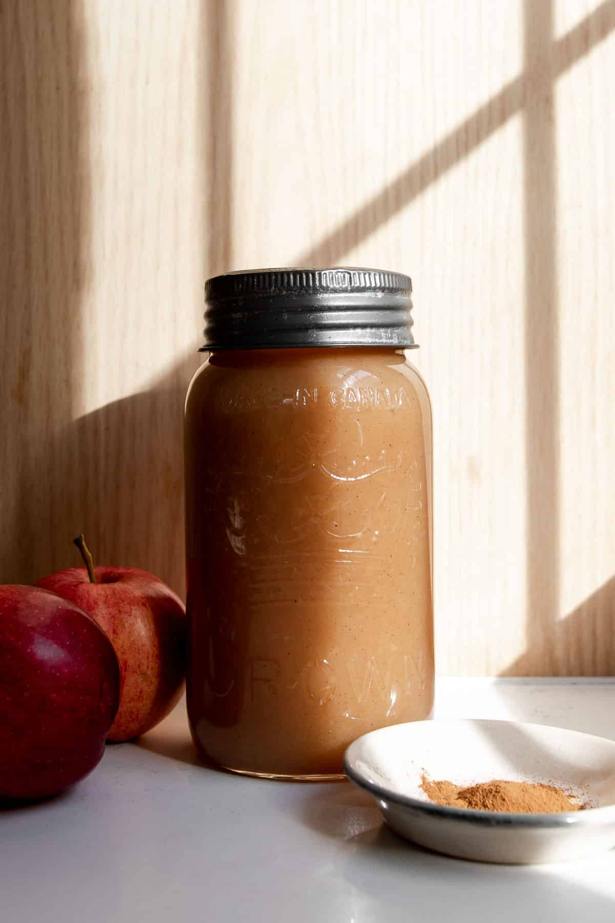 applesauce in a jar with apples and cinnamon next to it in the sun.
