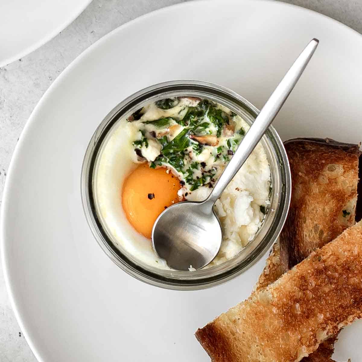 coddled eggs in a mason jar with a spoon served with toast fingers.