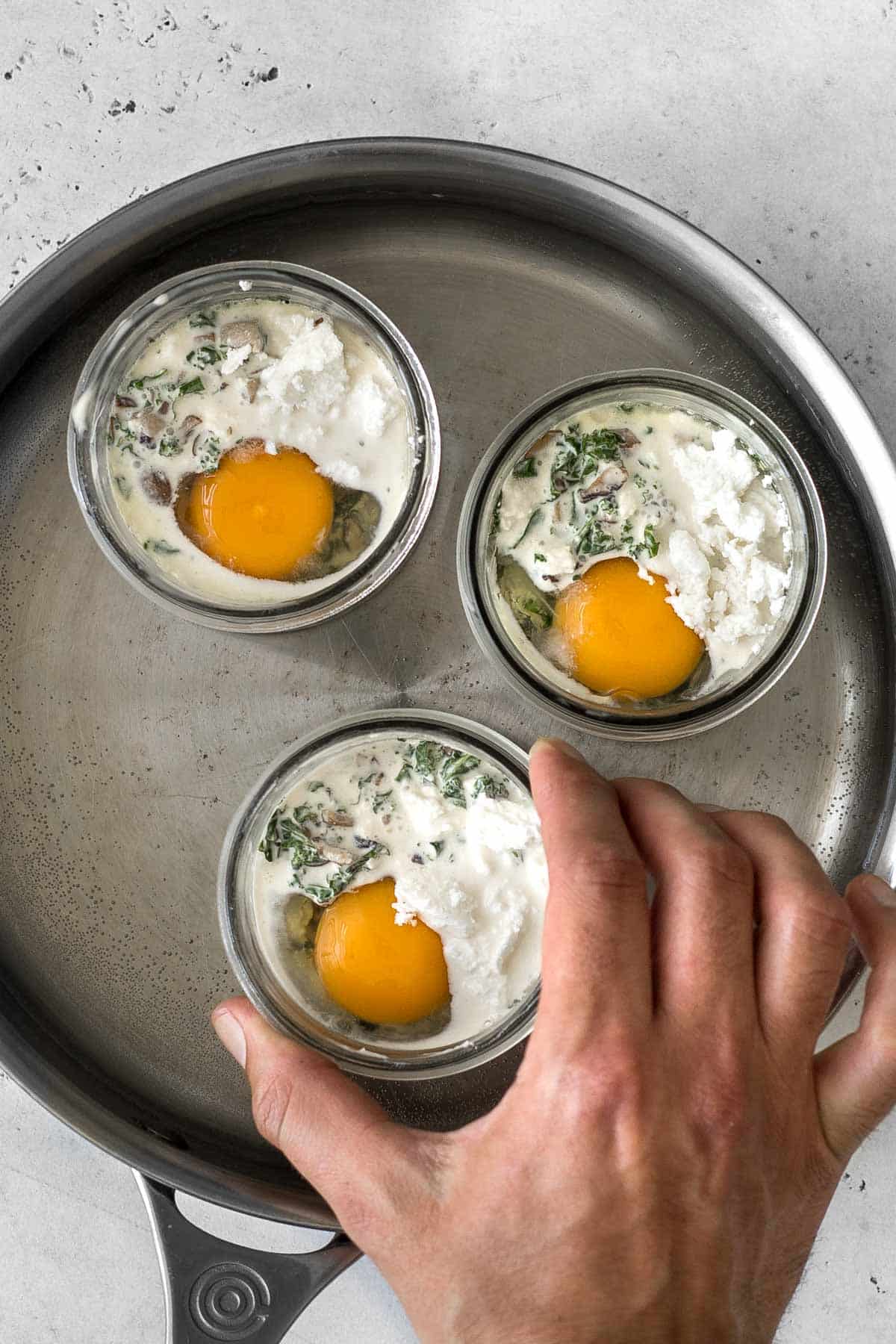 hand placing mason jar with egg and cream mixture into water bath in a pan.