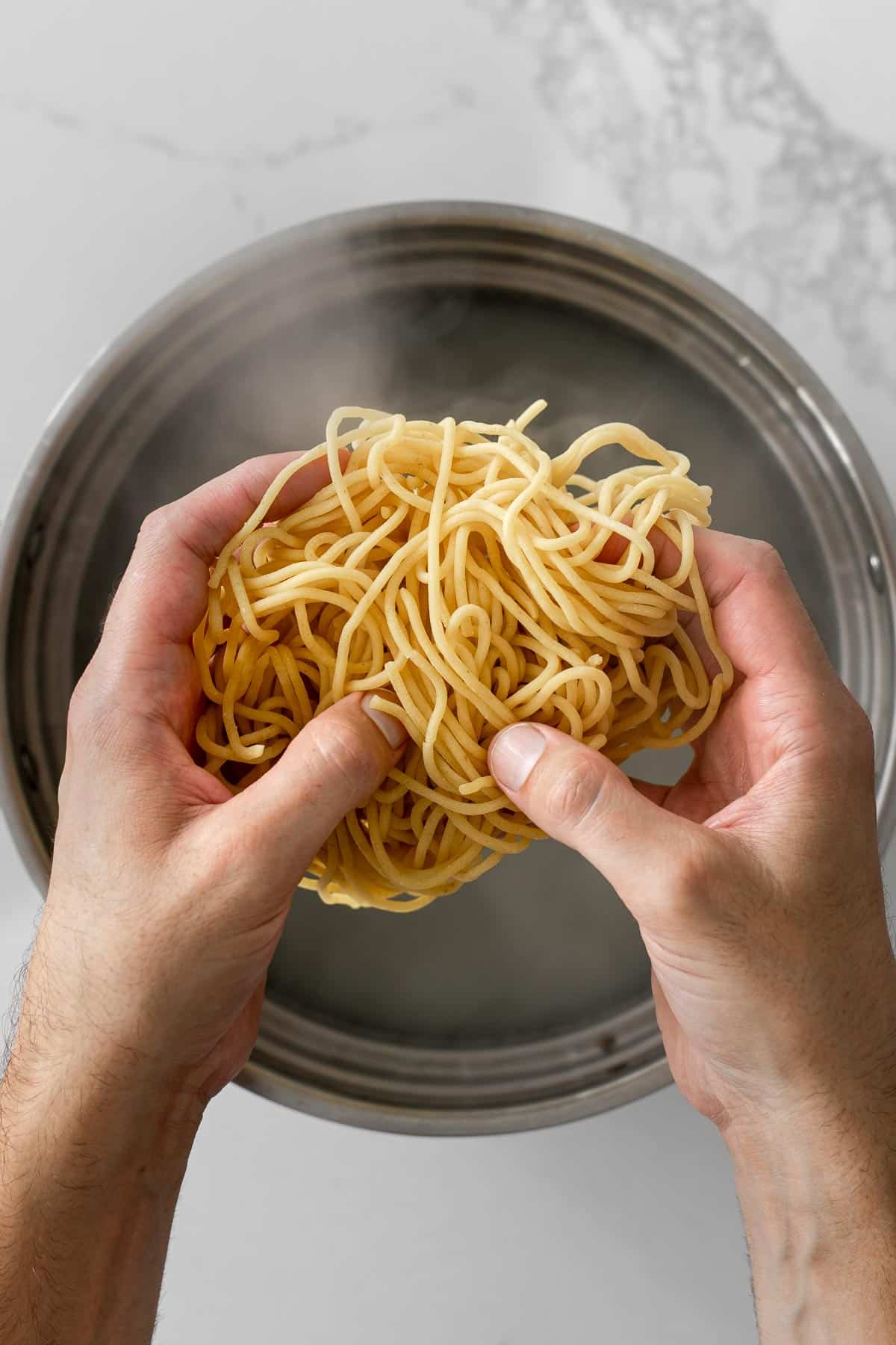 hands adding uncooked pasta to a pot of boiling water.