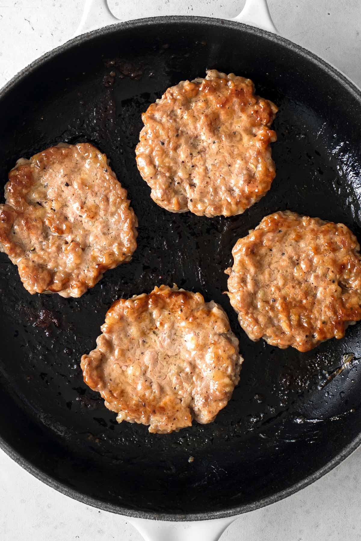 four sausage patties cooking in a skillet.