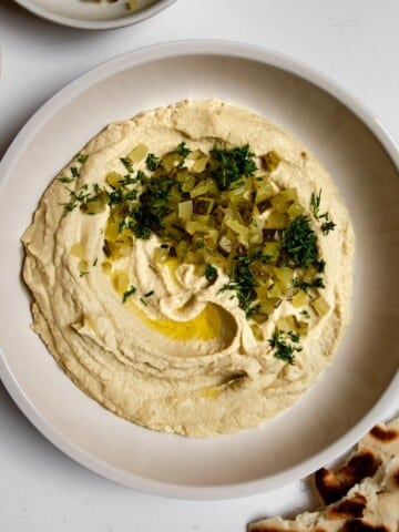 close up of hummus topped with chopped dill pickle and dill.