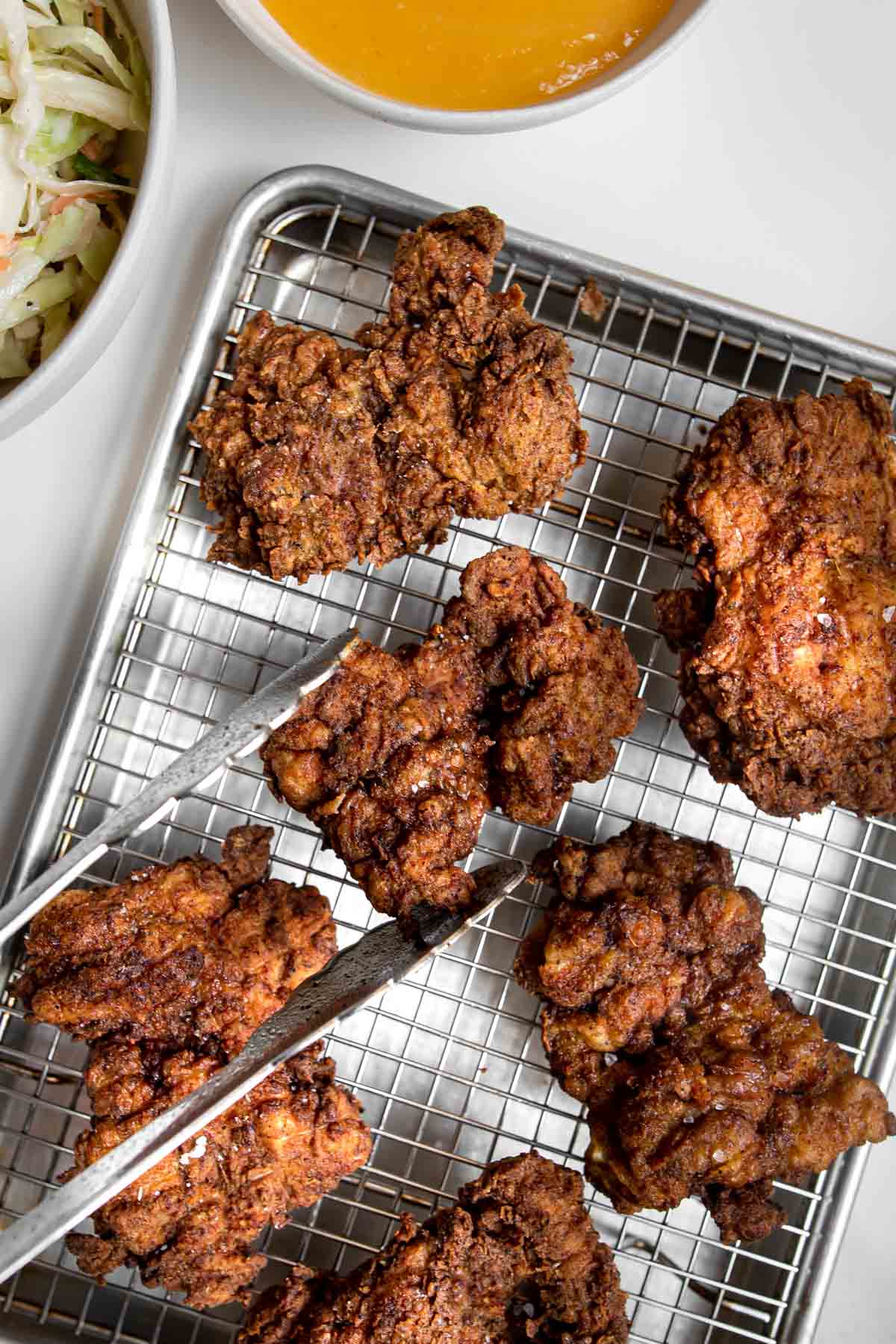 tongs placing a piece of curry fried chicken onto a cooling rack with other cooked chicken.