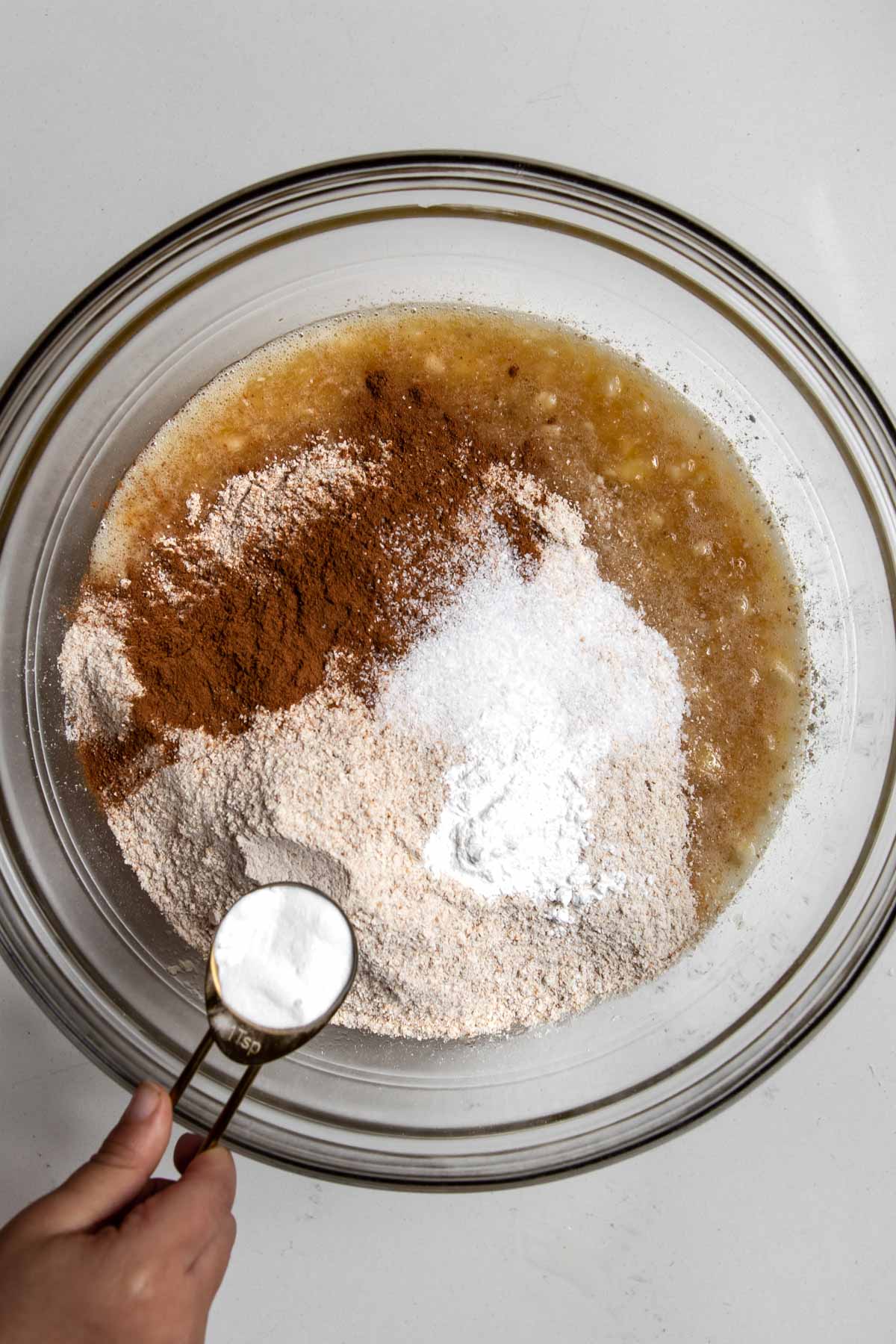 child hands adding dry ingredients to a bowl with wet ingredients.