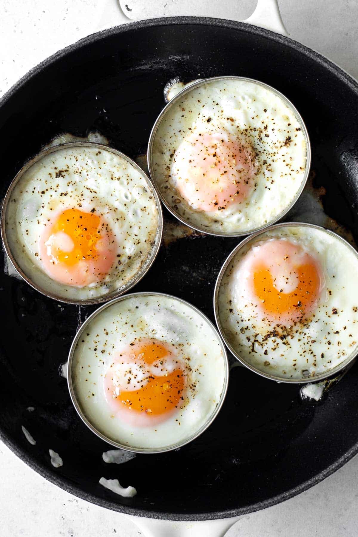 four eggs being cooked in molds in a skillet.