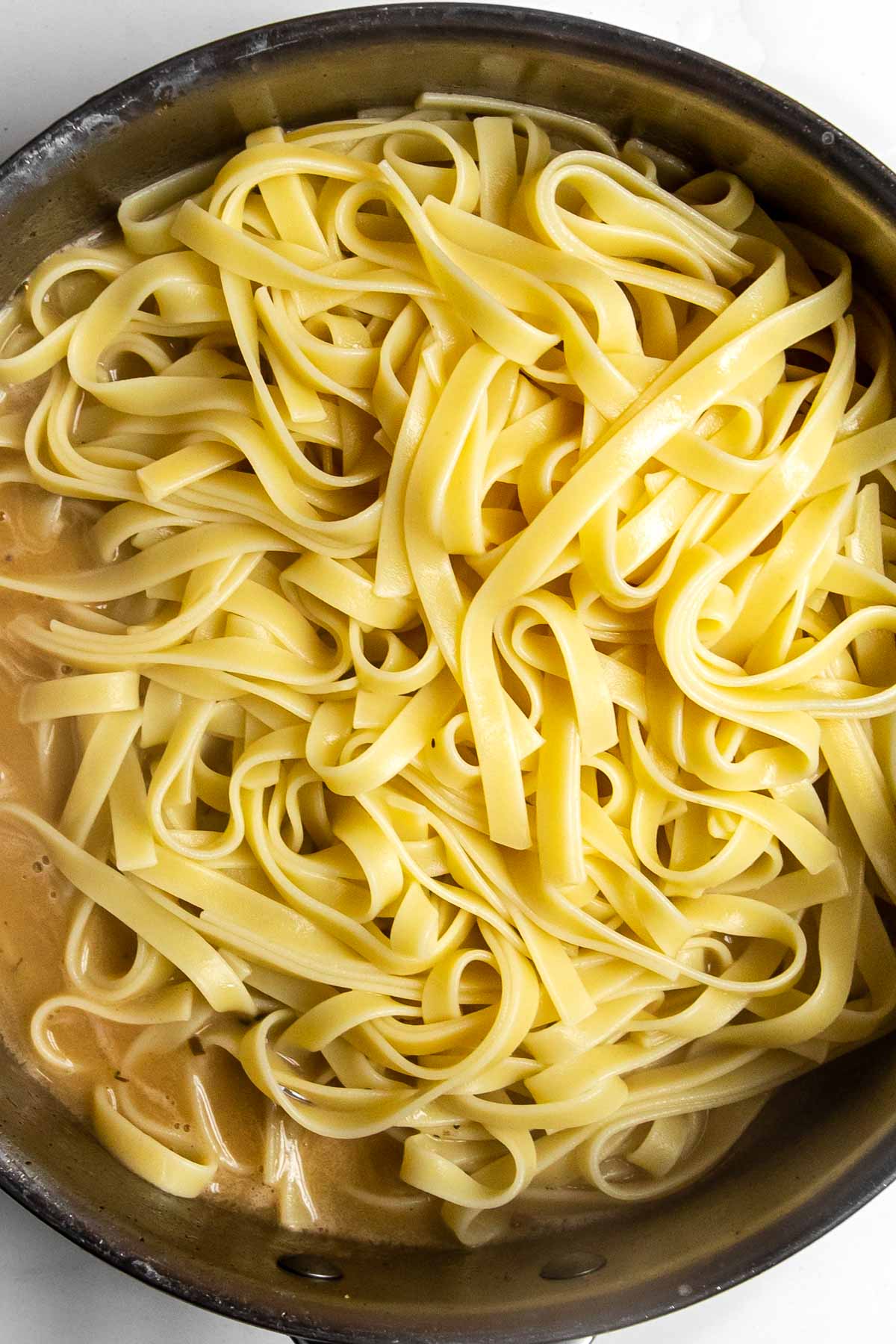 fettuccini noodles in a pan with emulsified butter and pasta water mixture.