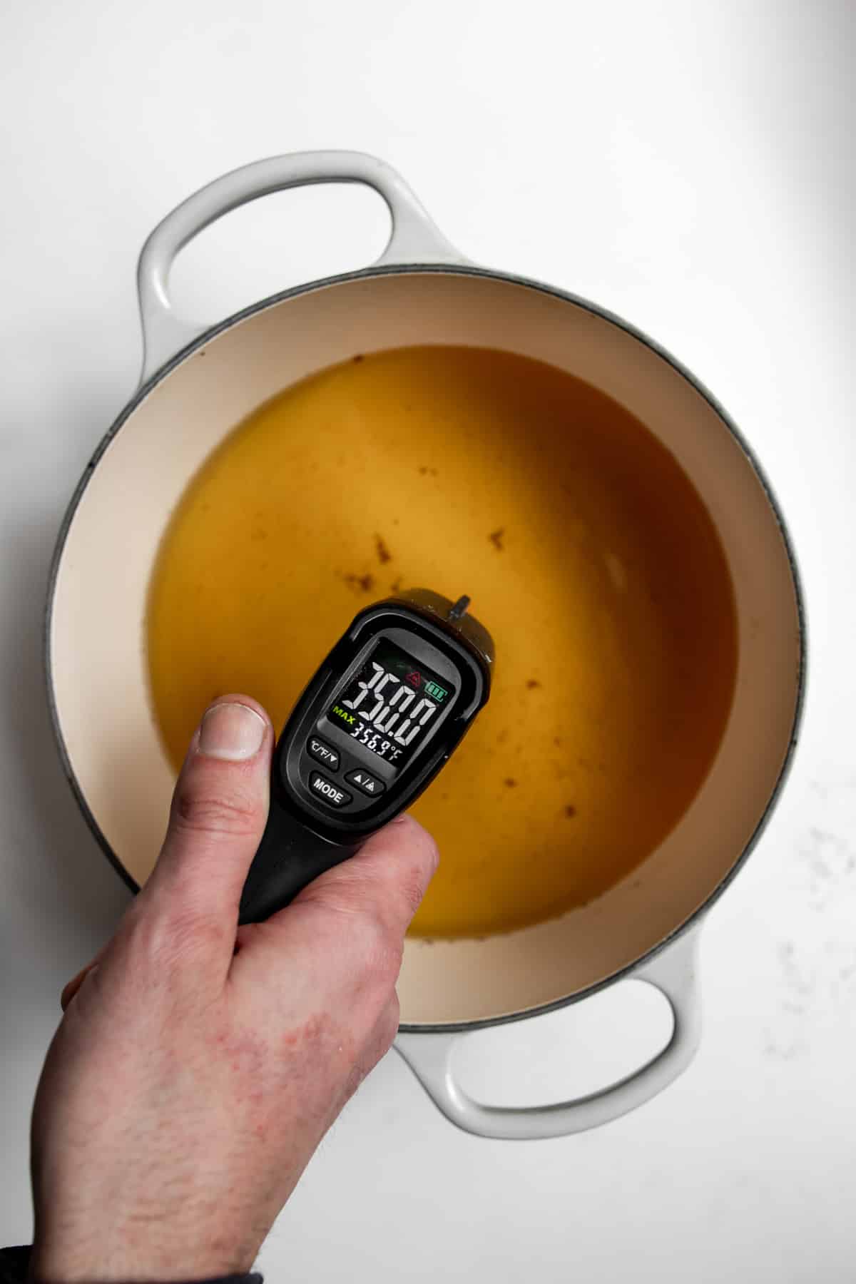 Hand holding laser thermometer reading 350°F over oil.
