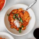 creamy gnocchi with vodka sauce in a bowl with a glass of wine next to it.