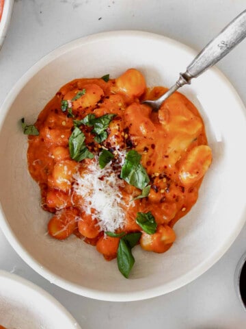 creamy gnocchi with vodka sauce in a bowl with a glass of wine next to it.