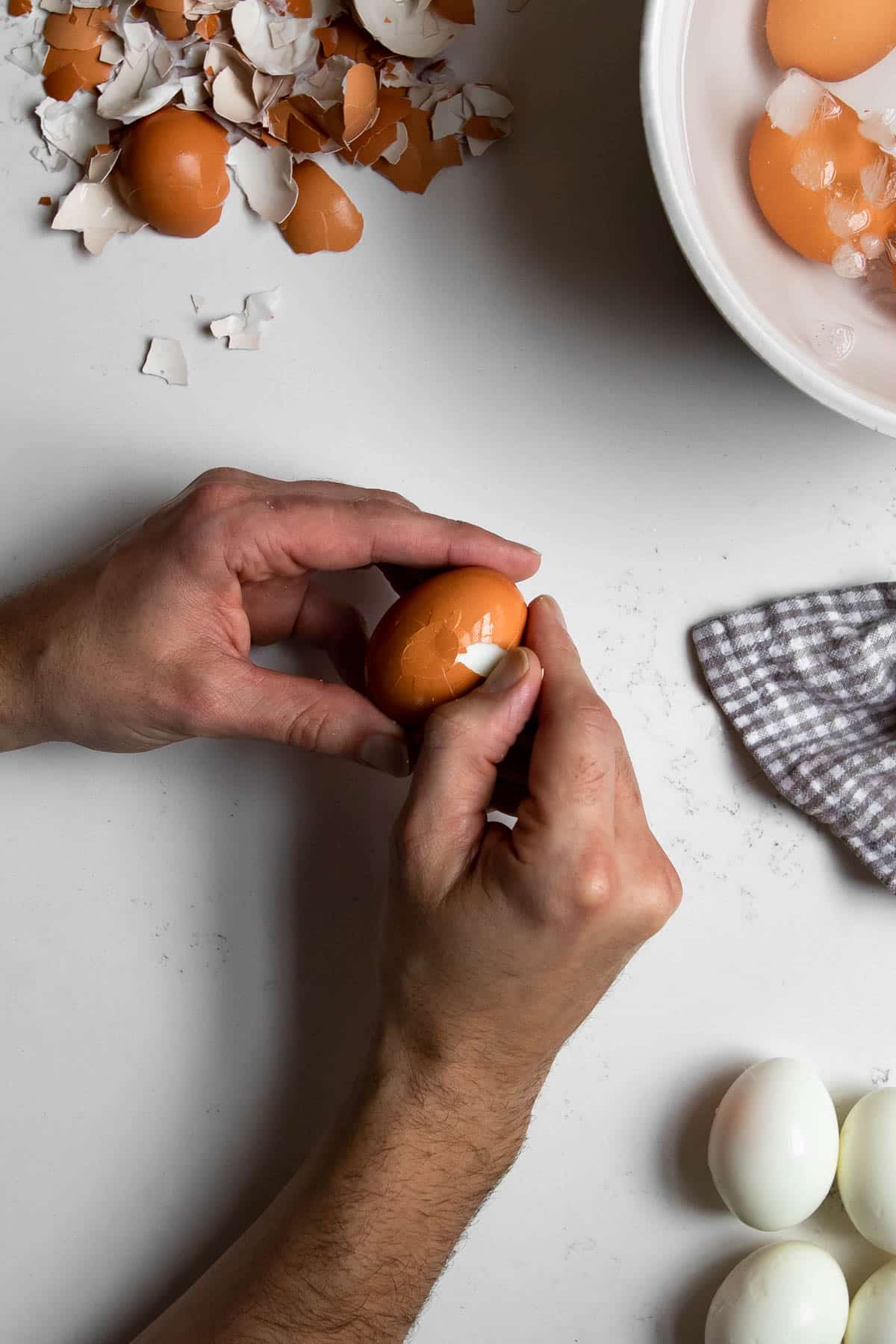 hand cracking the shell off of a hard boiled egg with shells around it.