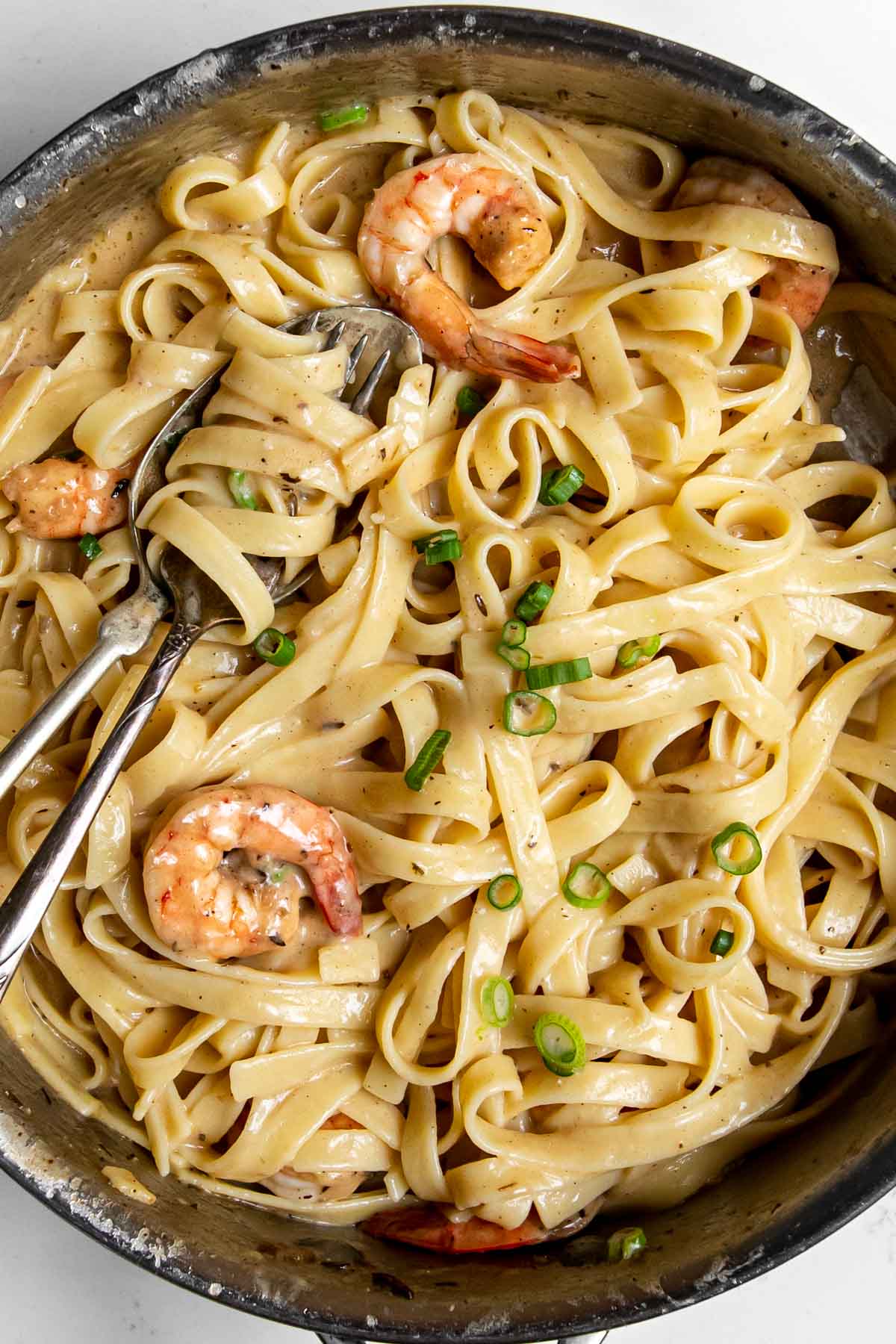 fettuccini Alfredo in a jerk cream sauce garnished with shrimp and green onions in a pan.