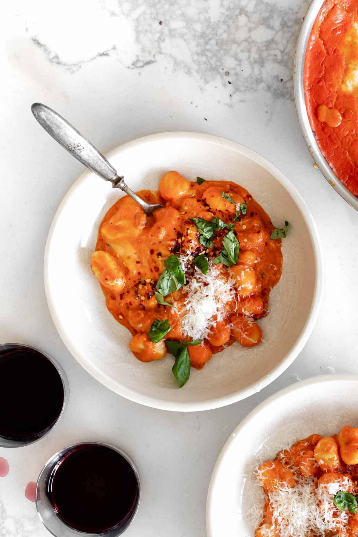 creamy gnocchi with vodka sauce in a bowl with two glasses of wine next to it.