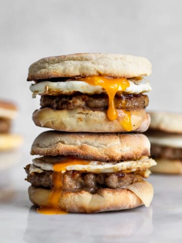 Two sausage, egg and cheese breakfast sandwich on an english muffin stacked on top of each other with yolk running down.