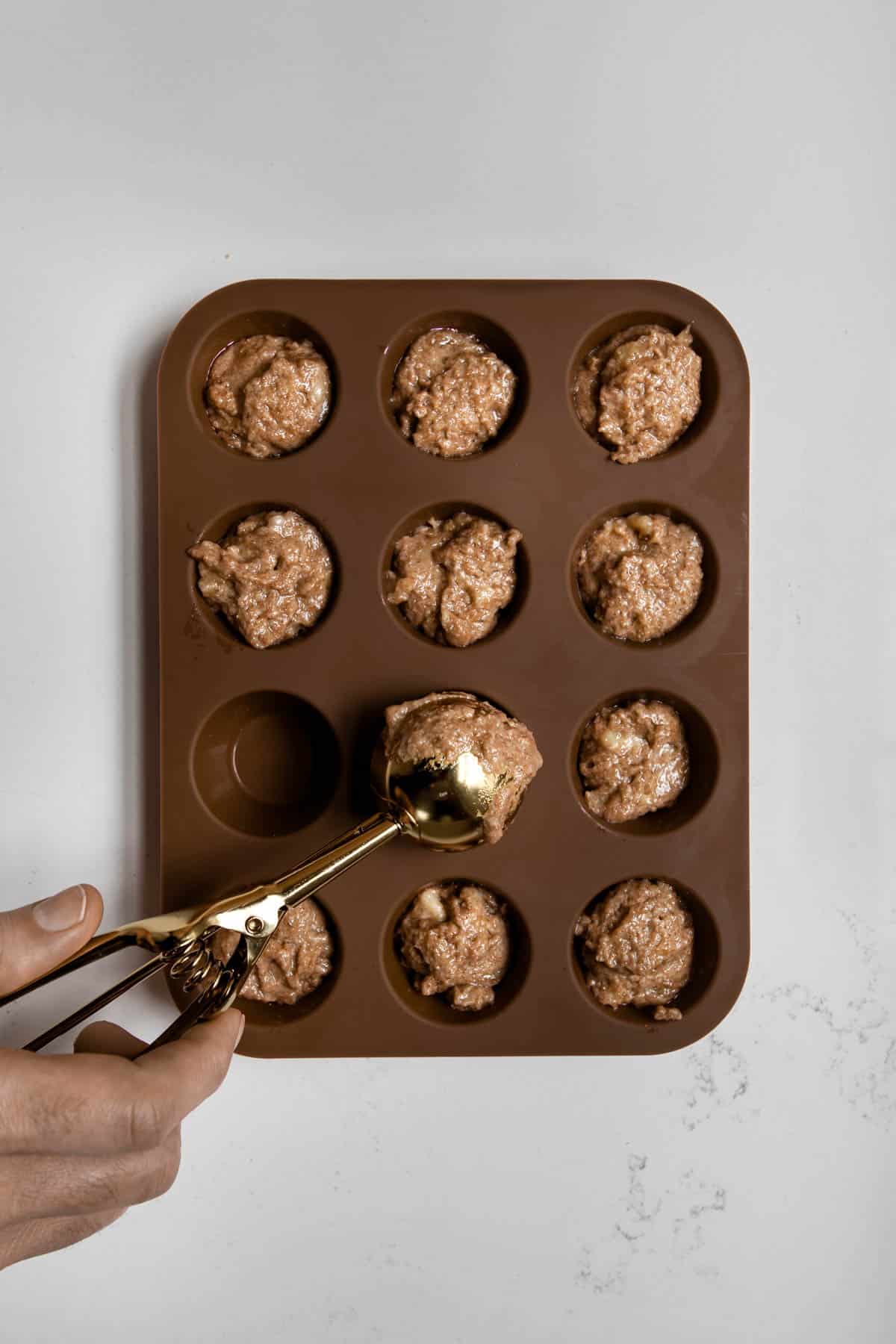 hand scooping banana batter into silicone mini muffin pan.