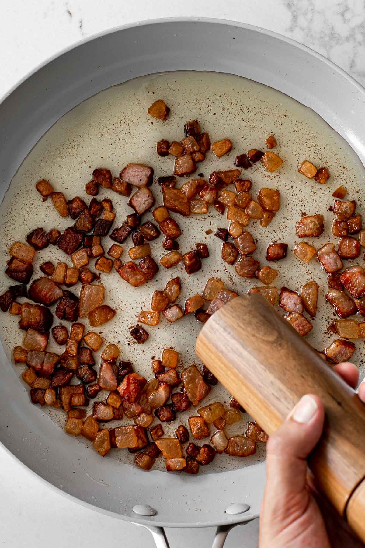 cooked guanciale in a pan being seasoned with black pepper.