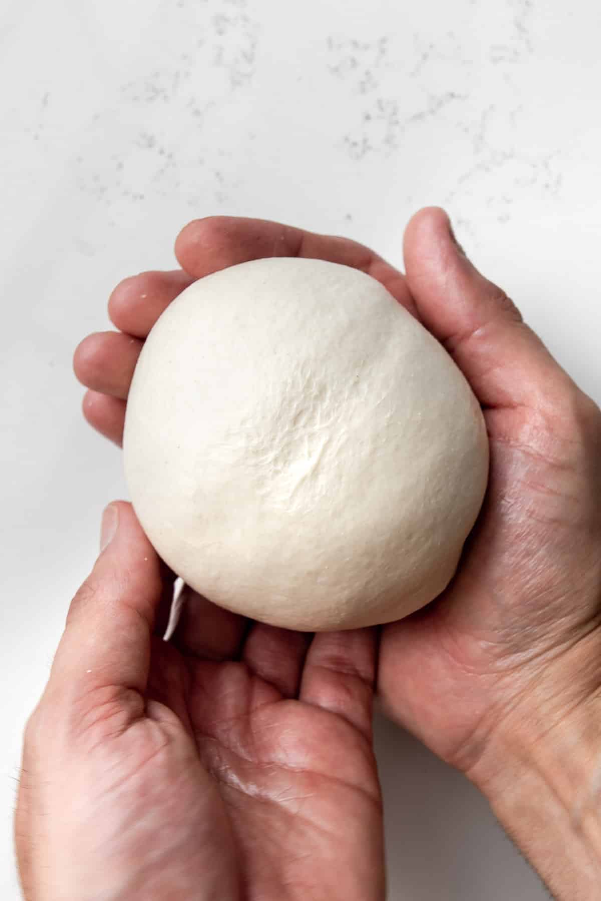hand holding a ball of pizza dough.