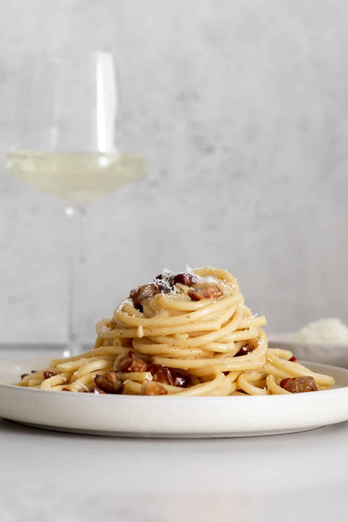 pile of carbonara on a plate with a glass of white wine.