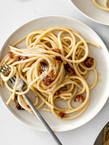 a plate of carbonara on a white table with a fork.