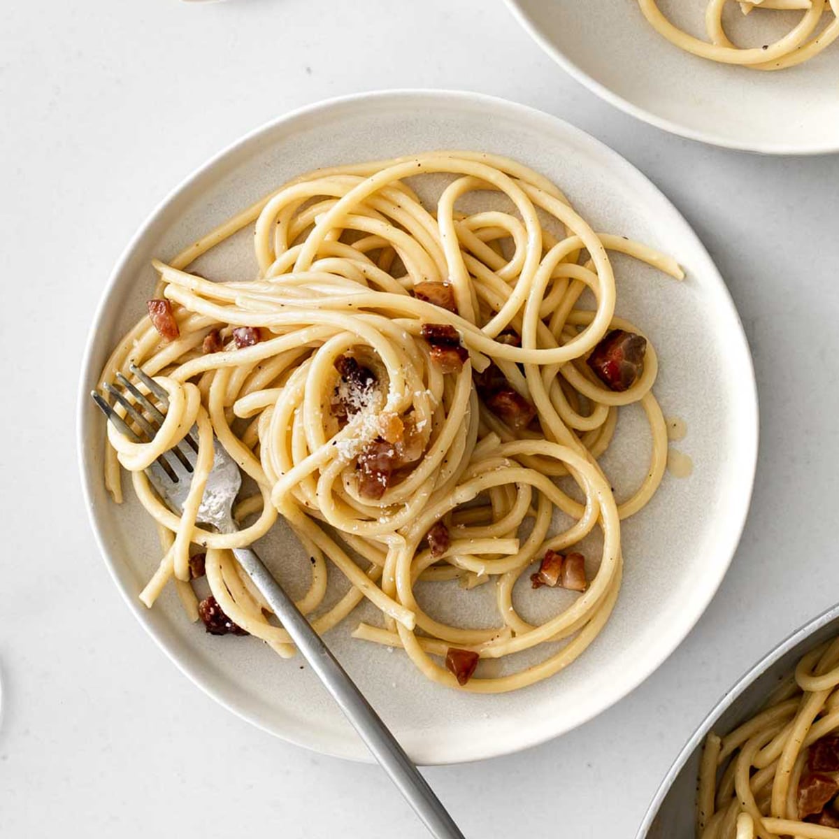 a plate of carbonara on a white table with a fork.