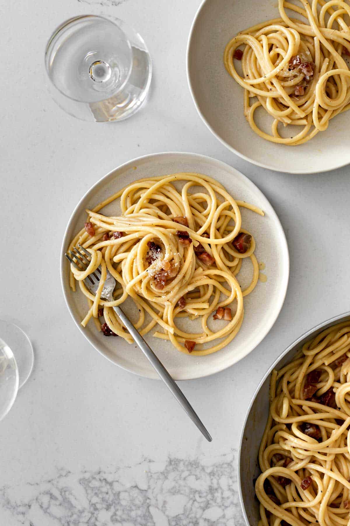 two plates of carbonara served with a glass of white wine.